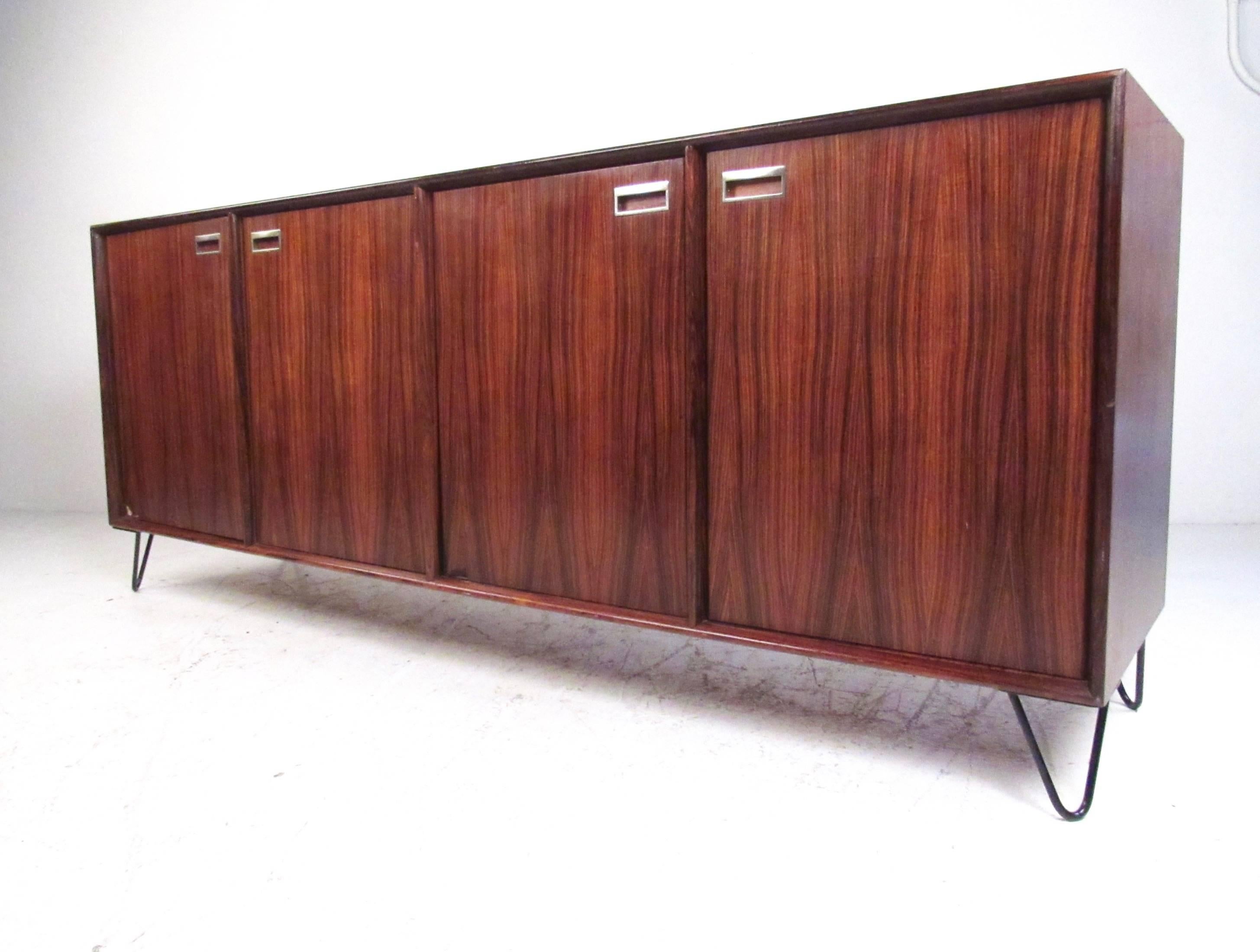 This stylish vintage sideboard features Scandinavian Modern style, impressive rosewood veneer, and spacious interior cabinets. Ideal for dining room storage or office use, this Mid-Century Modern piece boasts hairpin legs and carved wood pulls.