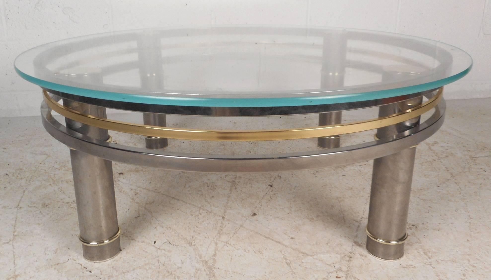 This elegant vintage modern coffee table features four thick cylindrical chrome legs with wraparound brass and chrome stretchers. Sleek design has a thick glass top with a light tint of green. Unique two-tone piece provides a sturdy and stylish