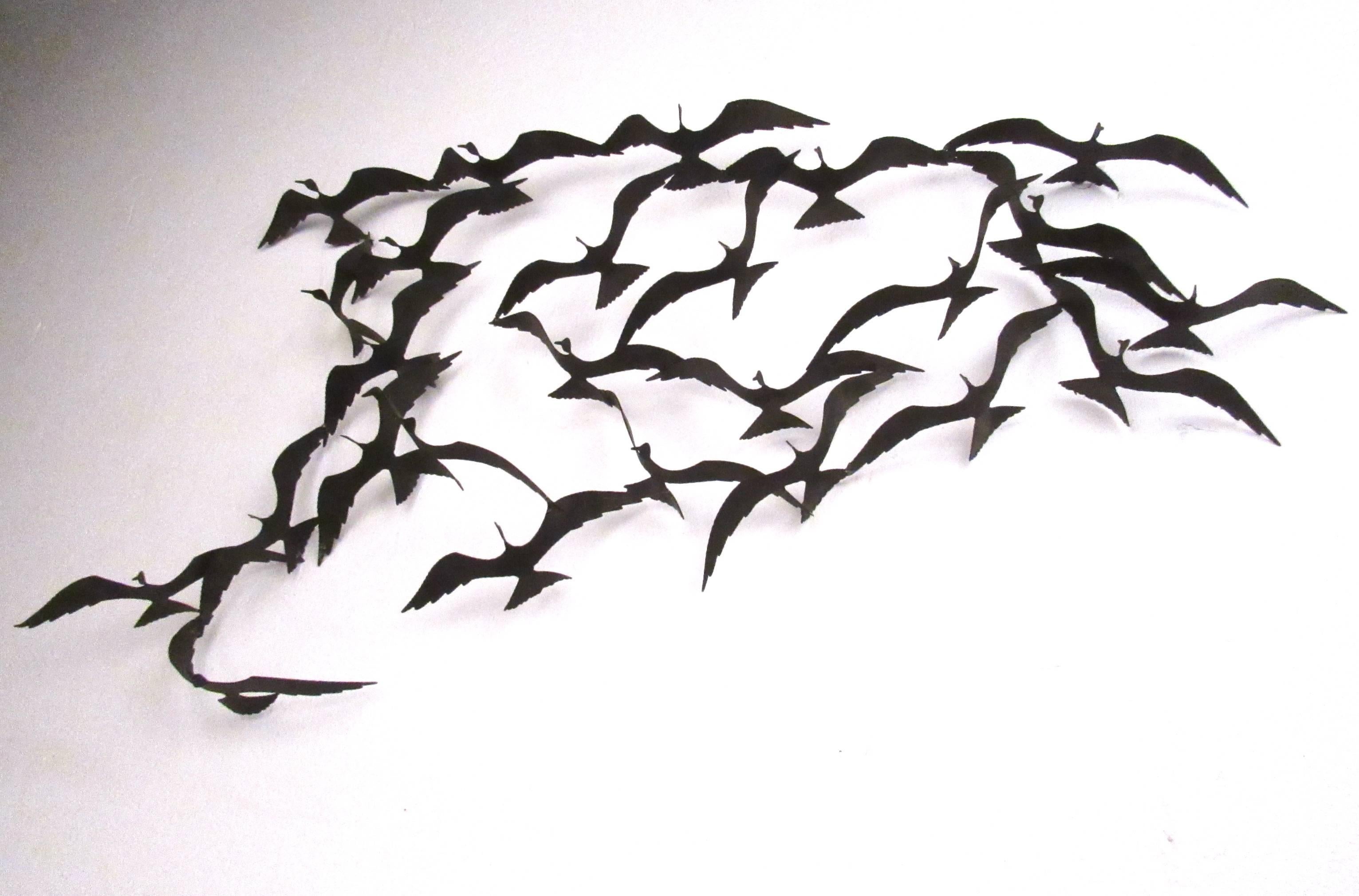 This contemporary modern wall art depicts a flock of flying birds in motion. Vintage style with a whimsical twist, this sculptural metal wall hanging makes a stylish addition to home or office decor. Please confirm item location (NY or NJ).