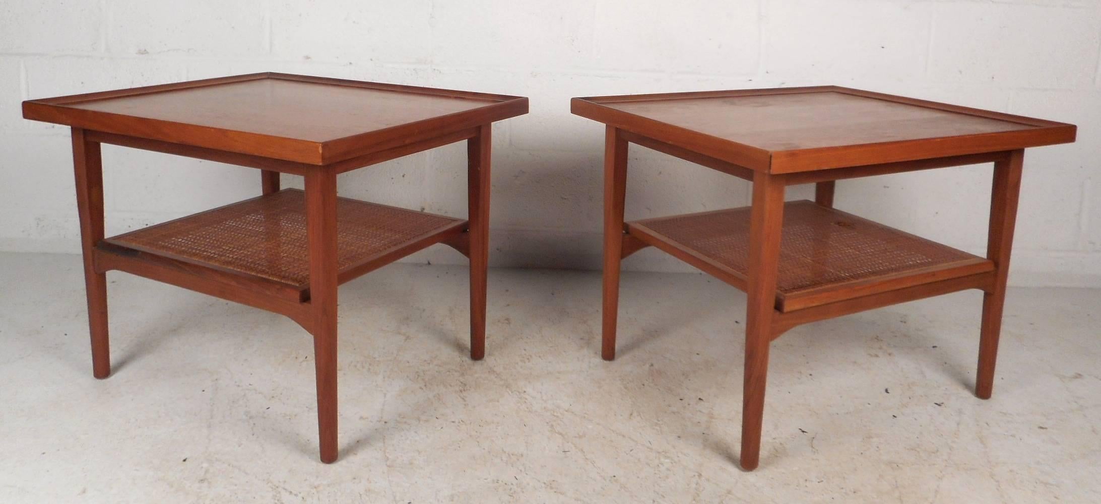Stunning pair of vintage modern side tables feature two tiers to store and set items on. Unique design has raised edges along the tabletop and a stylish lower cane shelf. Sturdy and stylish rectangular design with gorgeous walnut wood grain. These