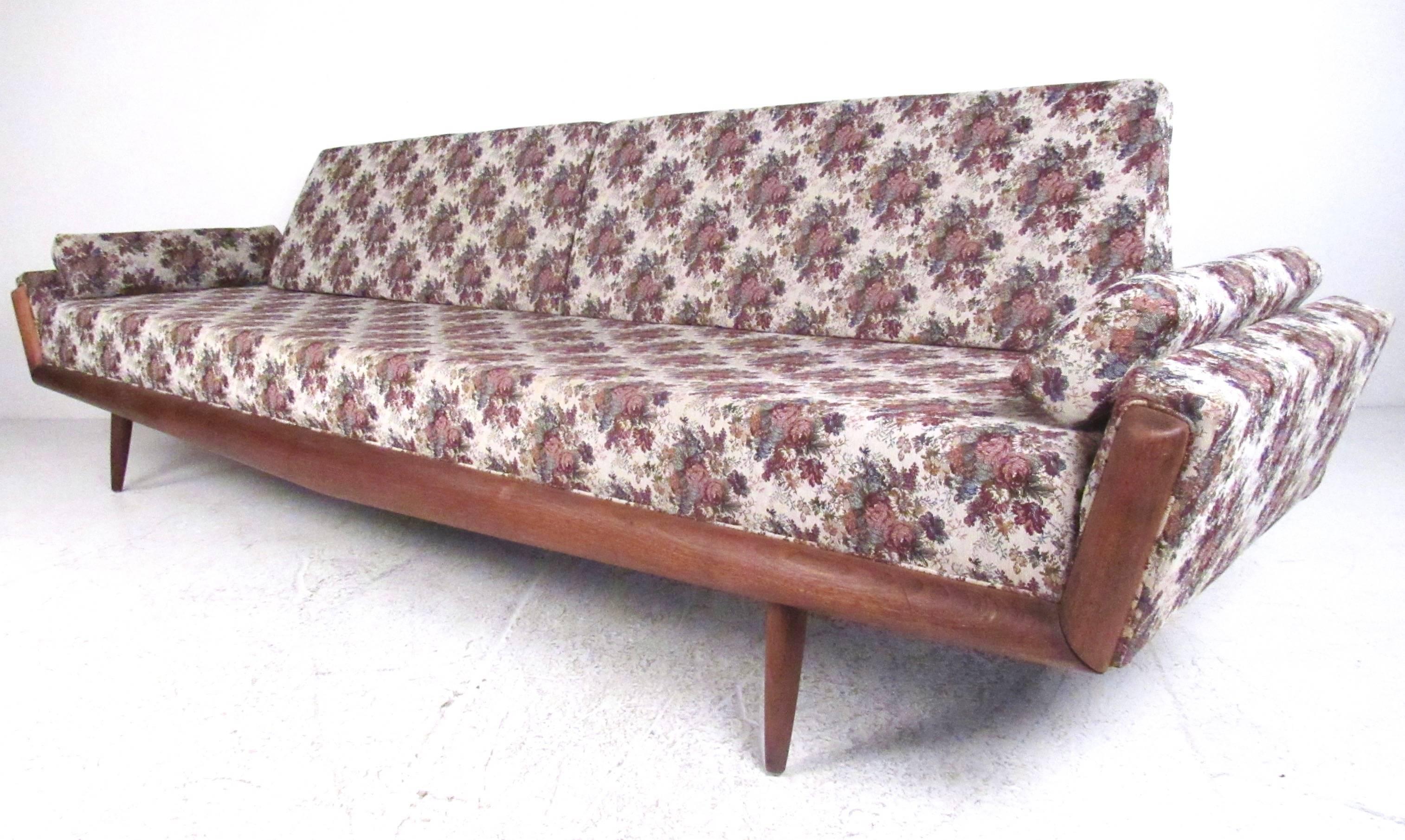 This unique Mid-Century sofa features a stylish walnut frame with unique sculpted armrests and seatback. Tapered hardwood legs complement the vintage modern floral covering, making it an impressive oversized seating option for home or business use.