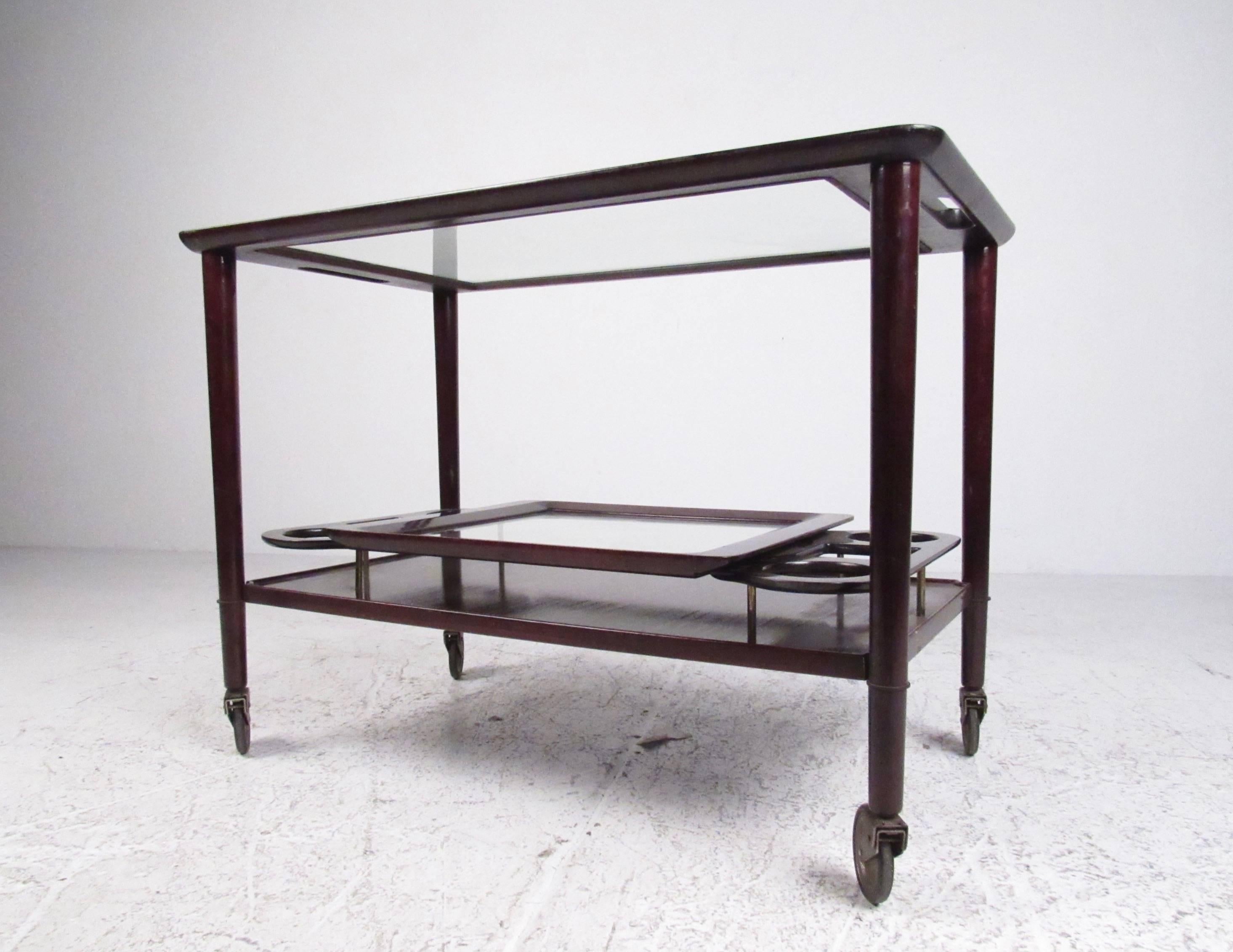 This unique Mid-Century Modern service cart features Italian mahogany construction, tapered/lacquered frame, and sturdy vintage casters. Glass top with matching removable tray offers a spacious and versatile service area perfect for use as a bar