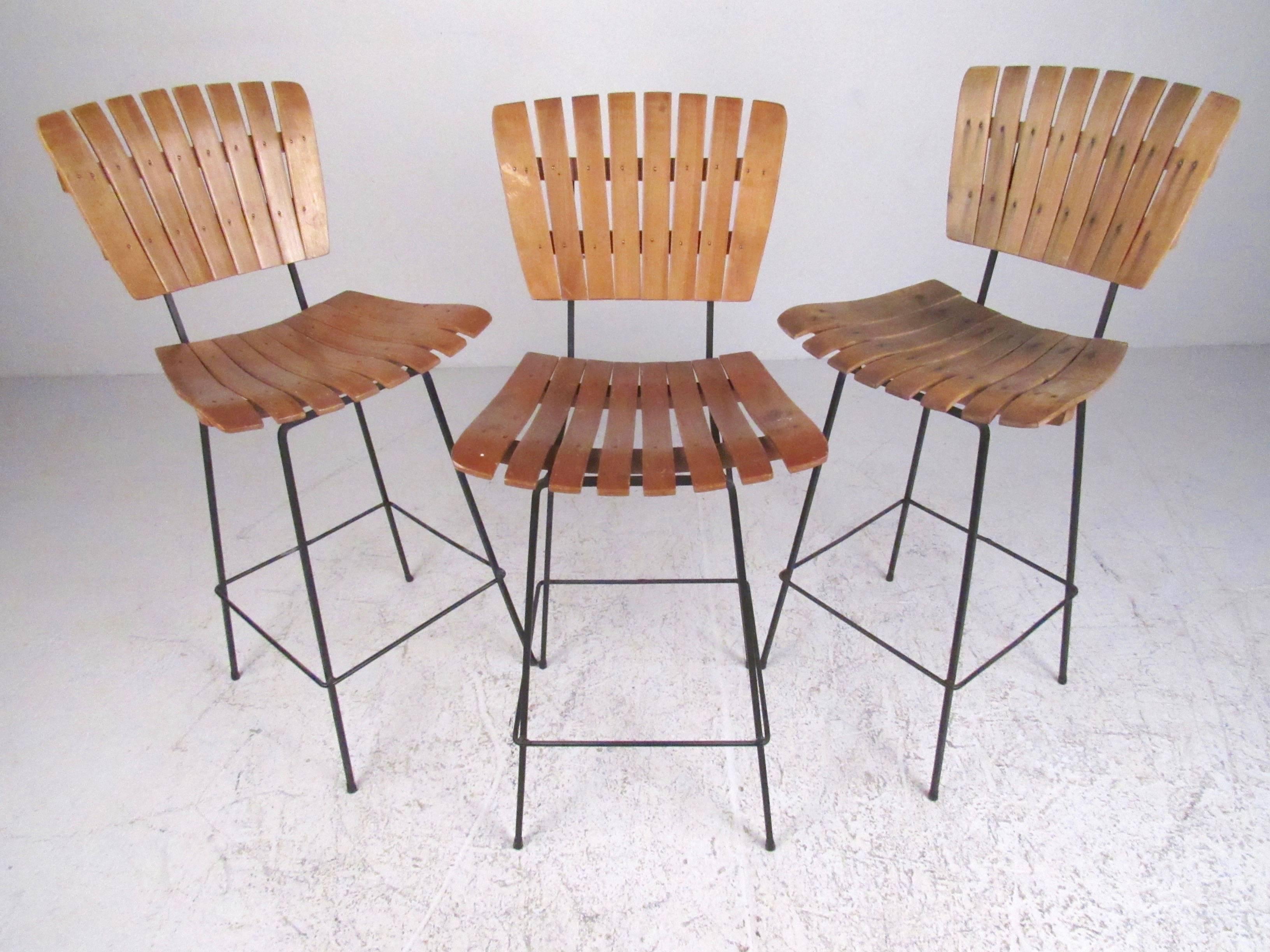 This set of three vintage modern slat style bar stools feature Arthur Umanoff style design, wood slat construction and cast iron metal bases. The sturdy set of three make a memorable mid-century addition to any interior. Please confirm item location