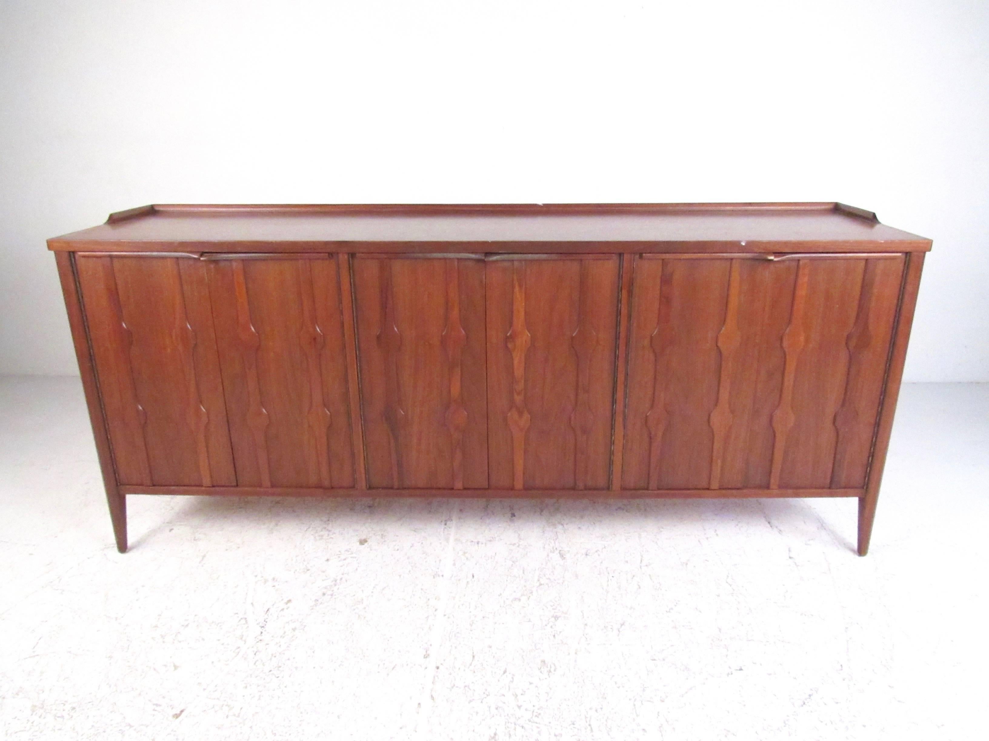 This vintage American sideboard features rich walnut finish, spacious interior cabinets, and stylish decorated cabinet doors. Raised edges and cared wood pulls combine with plenty of shelf and drawer space make this the perfect piece for dining room