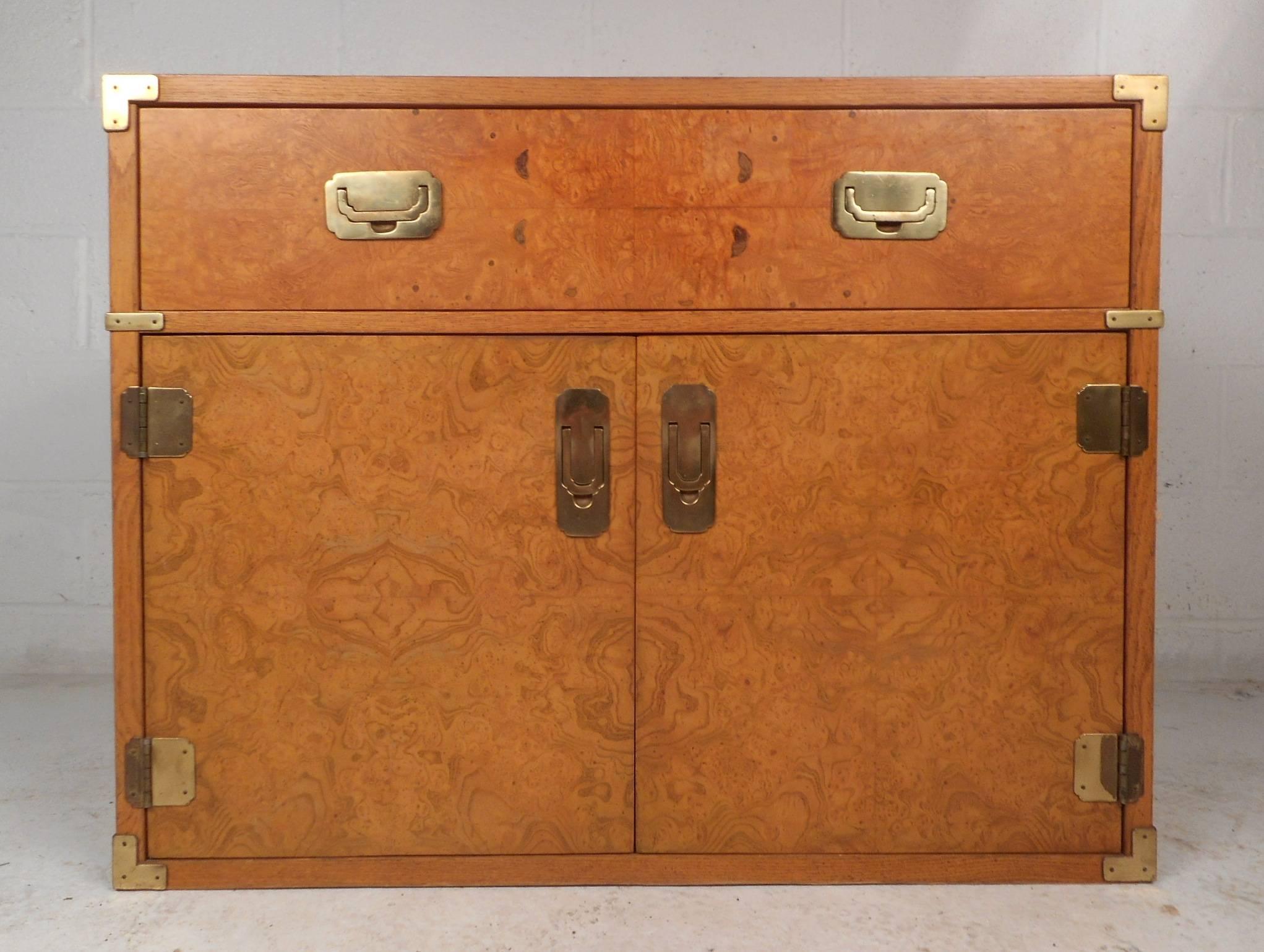 This stunning vintage modern Campaign chest features one large drawer and two cabinets that open to unveil a large compartment with a shelf. Elegant olive burl wood grain and unique brass pulls add to the allure. This unique case piece offers plenty