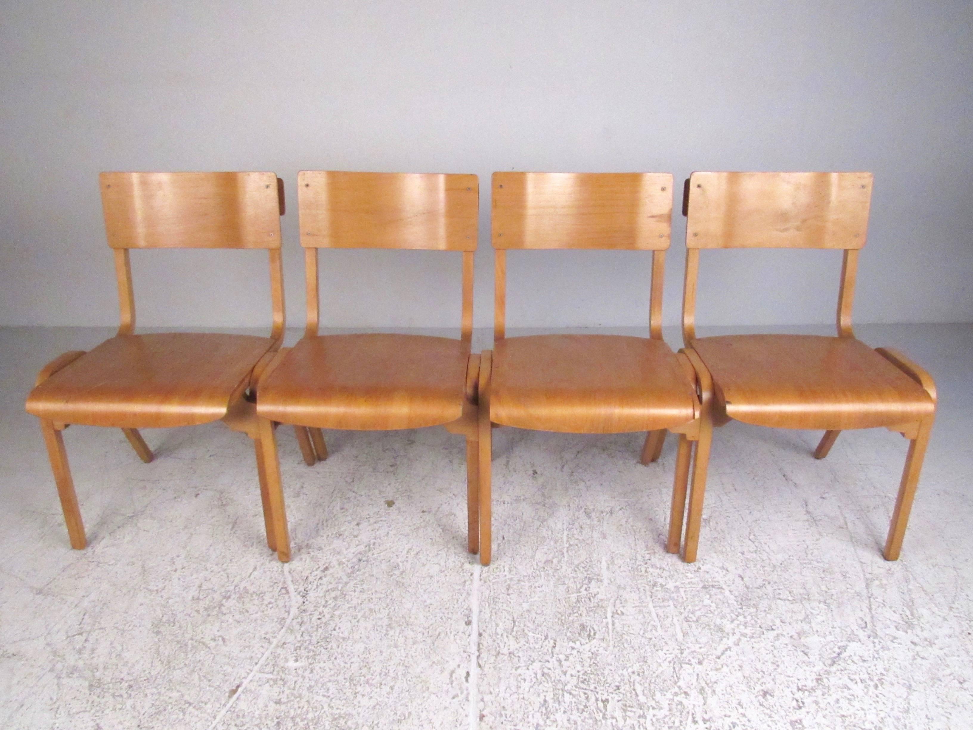 This unique set of four sculptural bentwood schoolroom chairs can be stacked or interlocked to create a four seat row or used separately as traditional dining chairs. Mid-century bentwood style and natural wood finish make these a memorable addition