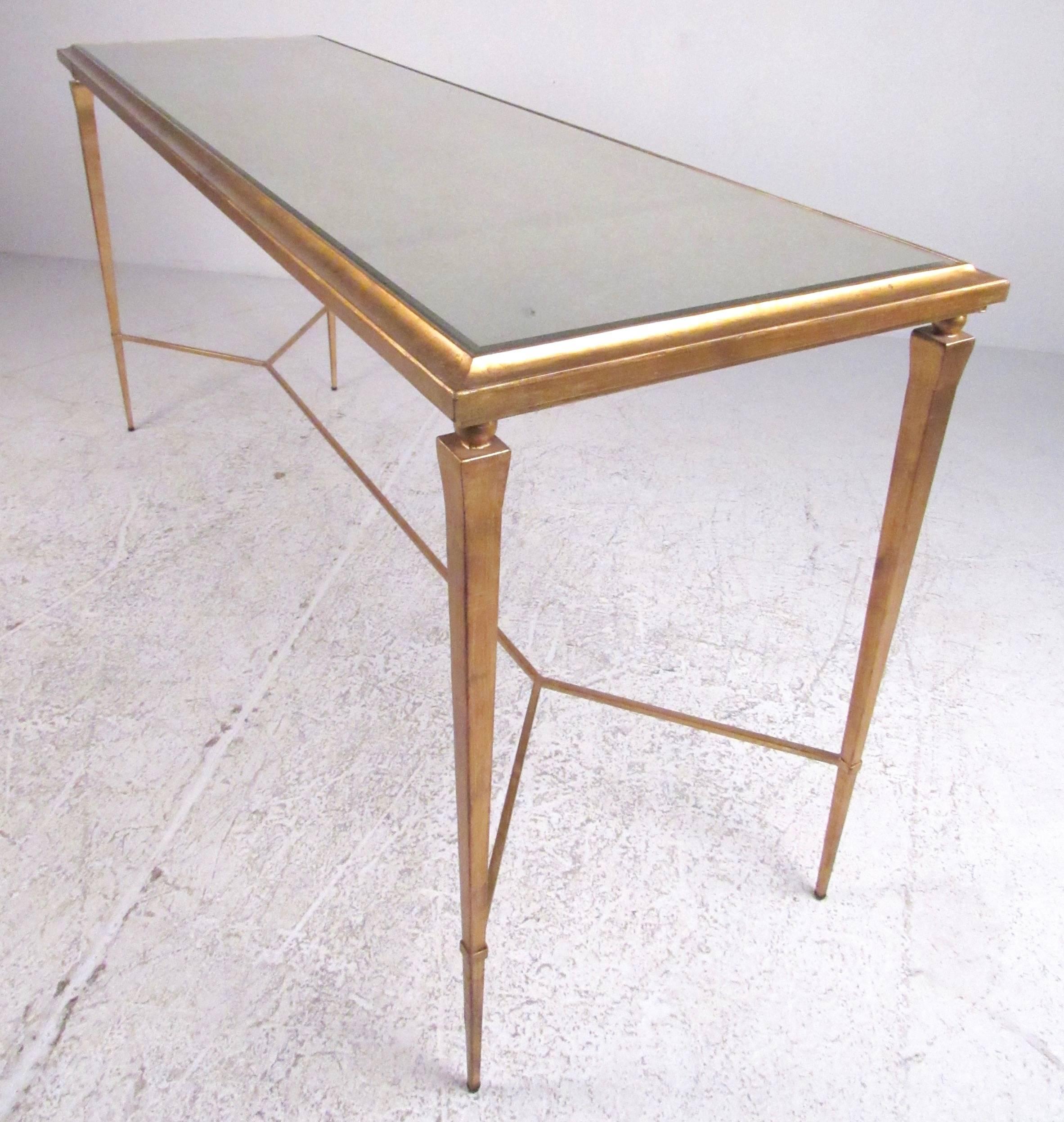 This ornate modern console table features gilded finish and tall, slender frame. Beveled mirror top has a unique antiqued finish, while the stylish design of this decorator console table makes it an impressive addition to any interior, perfect for