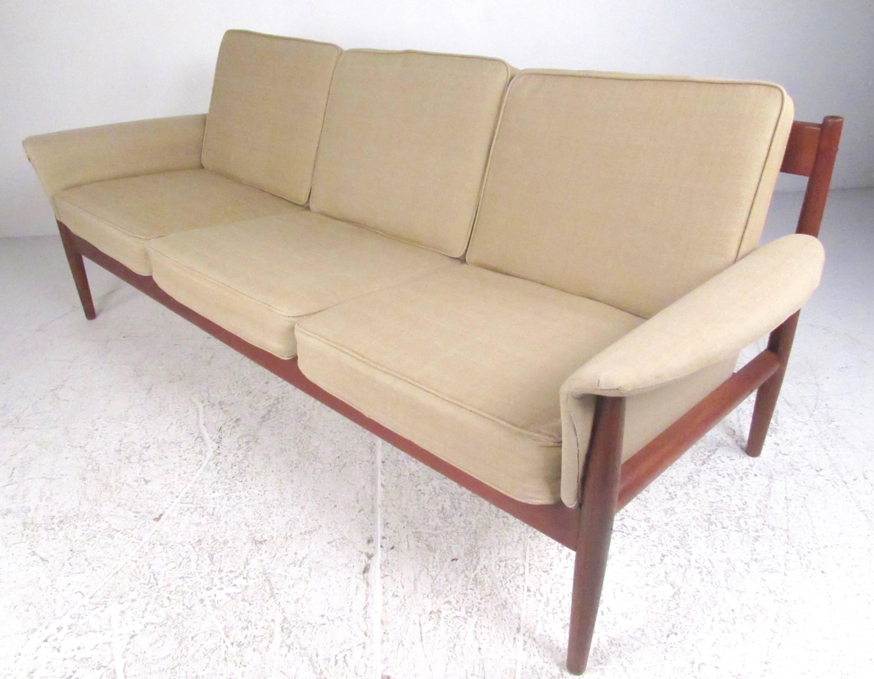 This stylish Mid-Century Modern teak sofa features comfortably upholstered three person seating, with sculpted teak frame and shapely upholstered armrests. This well-made vintage sofa was designed by Grete Jalk for France and Sons, please confirm