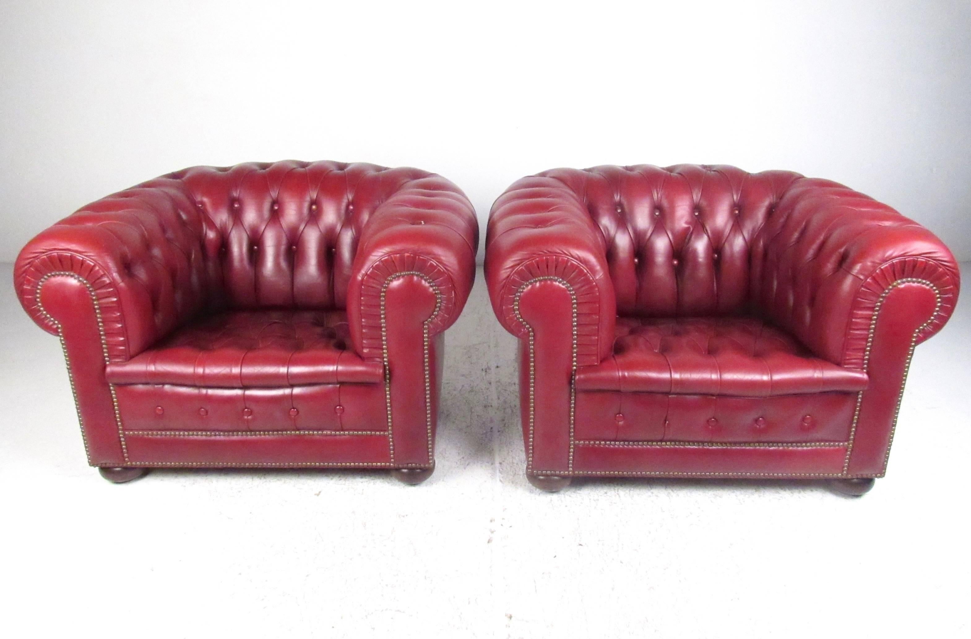 Cette élégante paire de fauteuils de salon Chesterfield présente un revêtement en cuir rouge sang-de-bœuf pelucheux, des sièges spacieux et confortables, et des pieds arrondis en bois dur. Les fauteuils club de grande qualité constituent un ajout