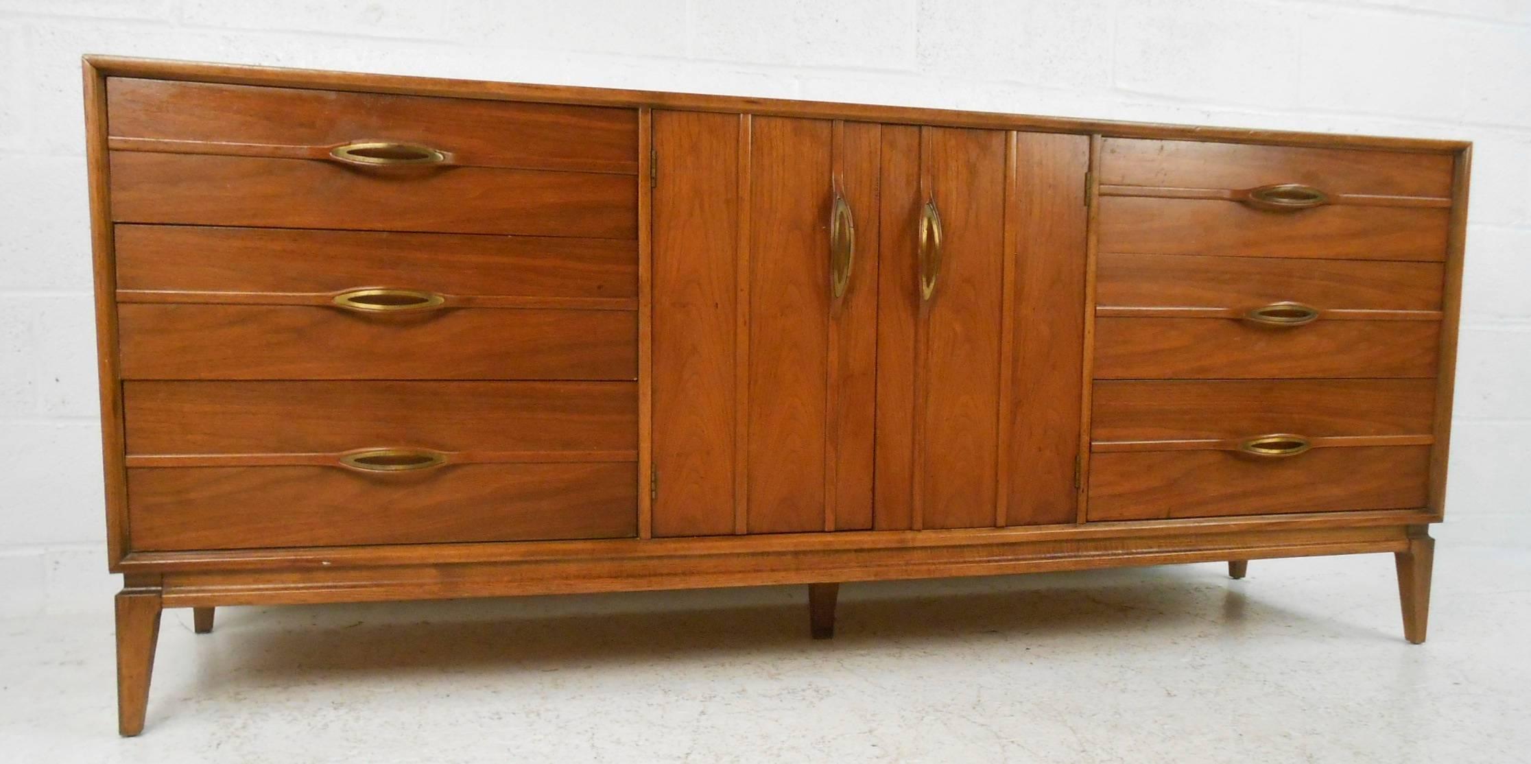 This gorgeous vintage modern dresser features unusual sculpted pulls on each drawer and cabinet. Sleek design provides plenty of room for storage within its nine hefty drawers. Sturdy construction with stunning walnut wood grain and splayed legs.
