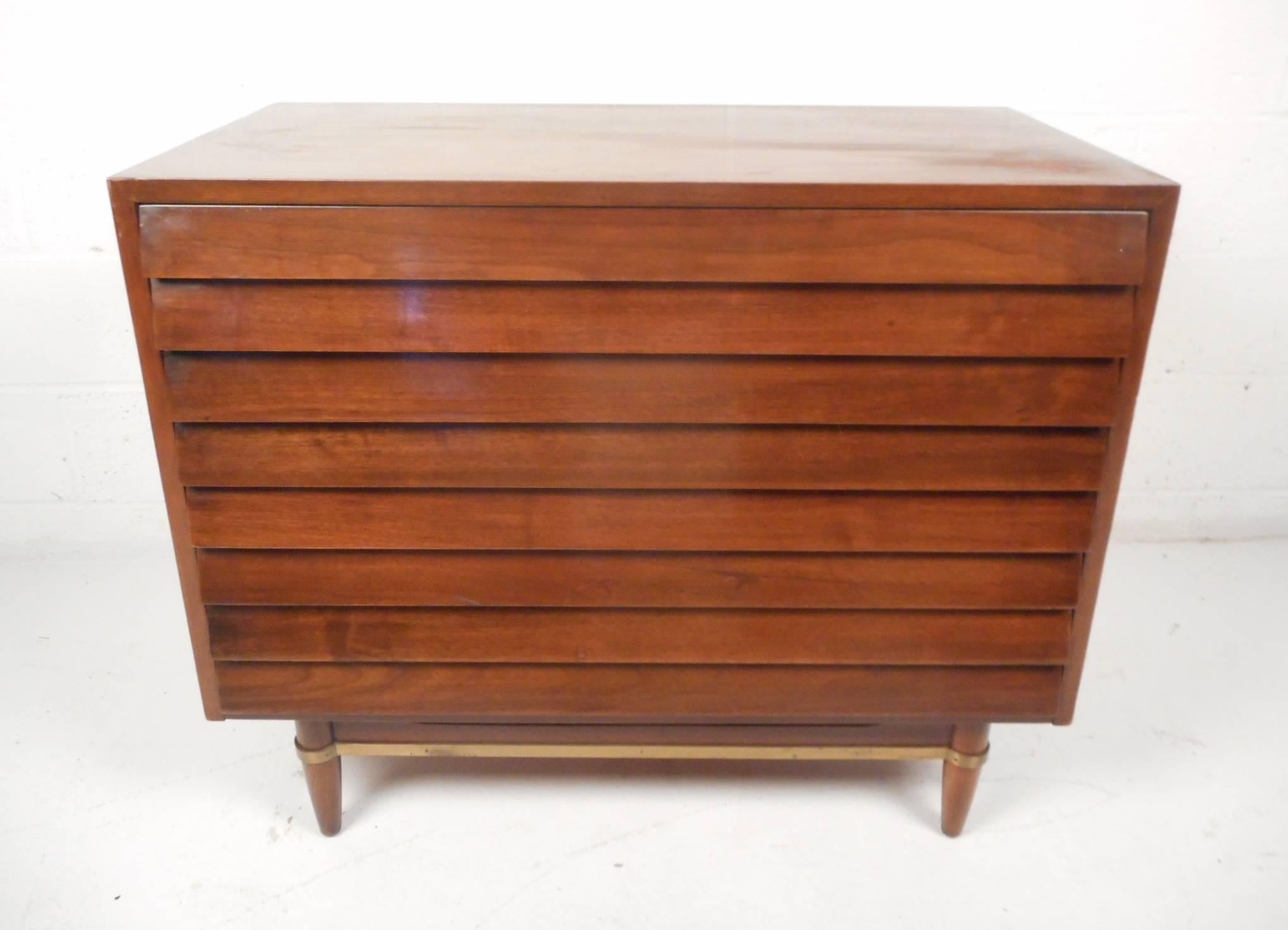 This beautiful vintage modern chest features three large drawers with louvered fronts which function has the pulls. Unique base with brass trim wrapping around the front and sides. Sturdy construction with lovely walnut wood grain sits on top of