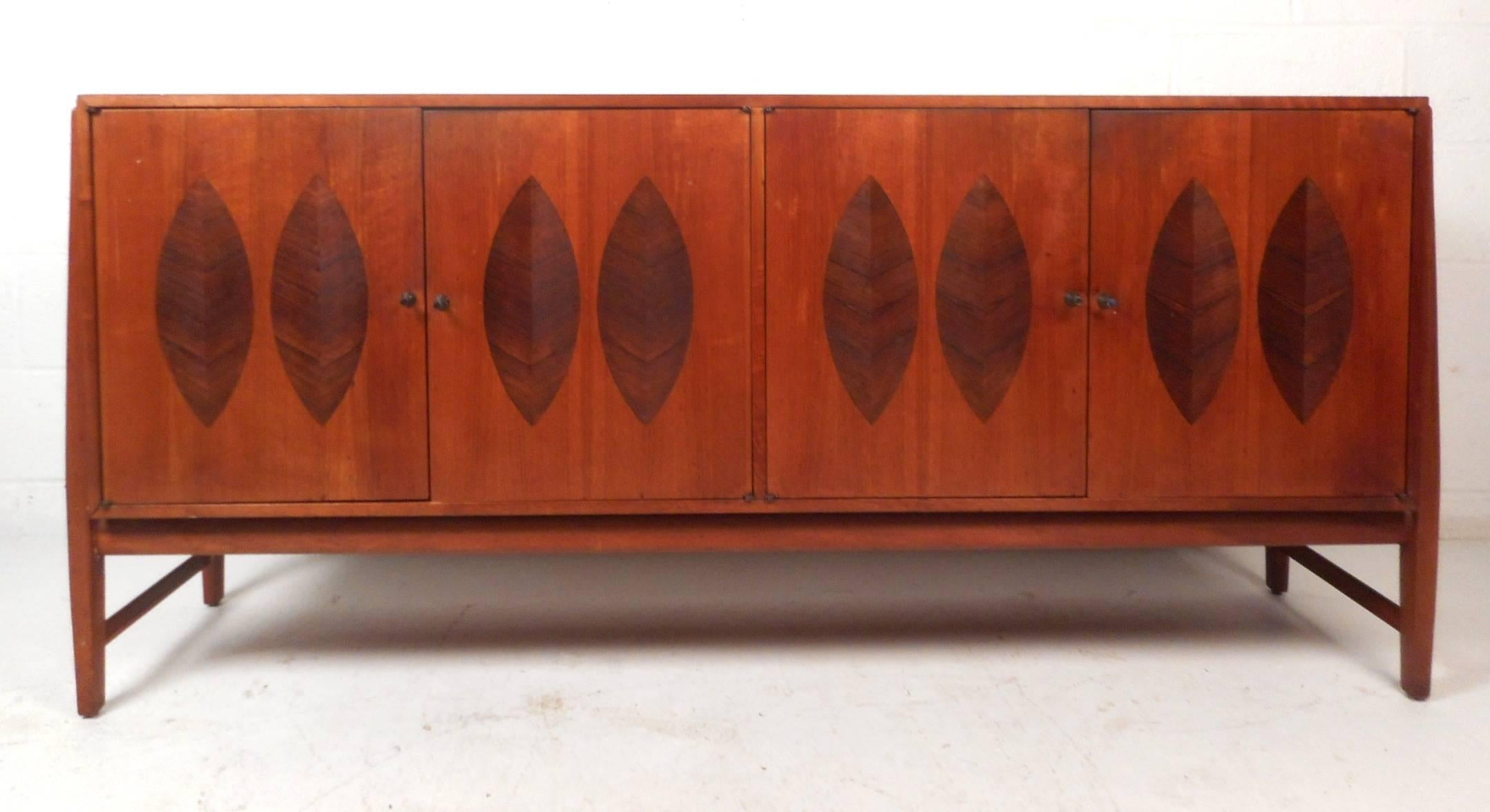 This amazing vintage modern sideboard features unique rosewood leaf inlays on the front of each cabinet door. Sleek design offers plenty of hidden storage space in its large compartments with drawers and a shelf. This lovely case piece has sculpted