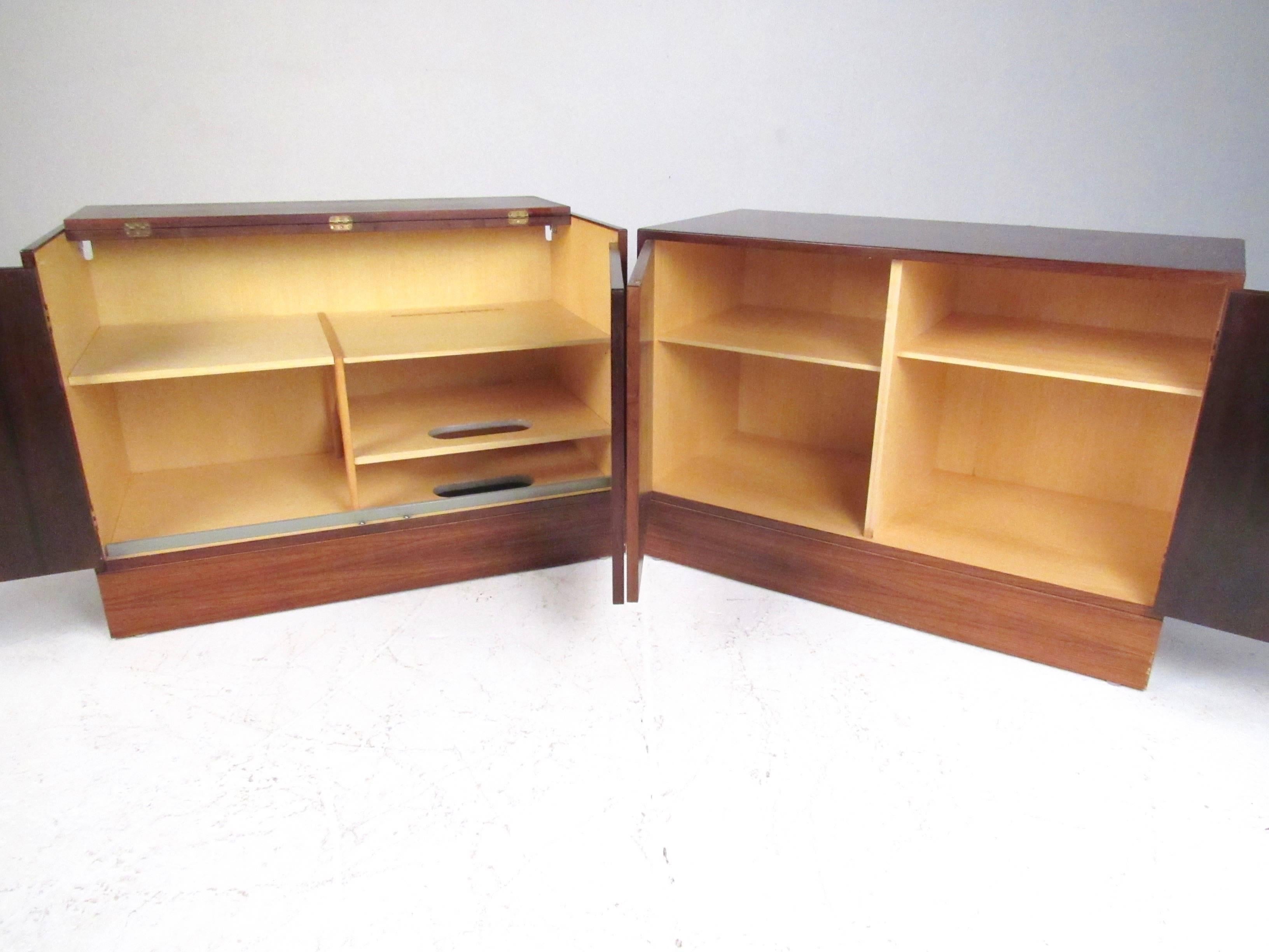 This exquisite pair of vintage modern cabinets feature a rich rosewood finish, beech interiors, and spacious storage options for any interior. Unique array of adjustable shelves and compartments, complete with cutaways for wiring. Carved door pulls