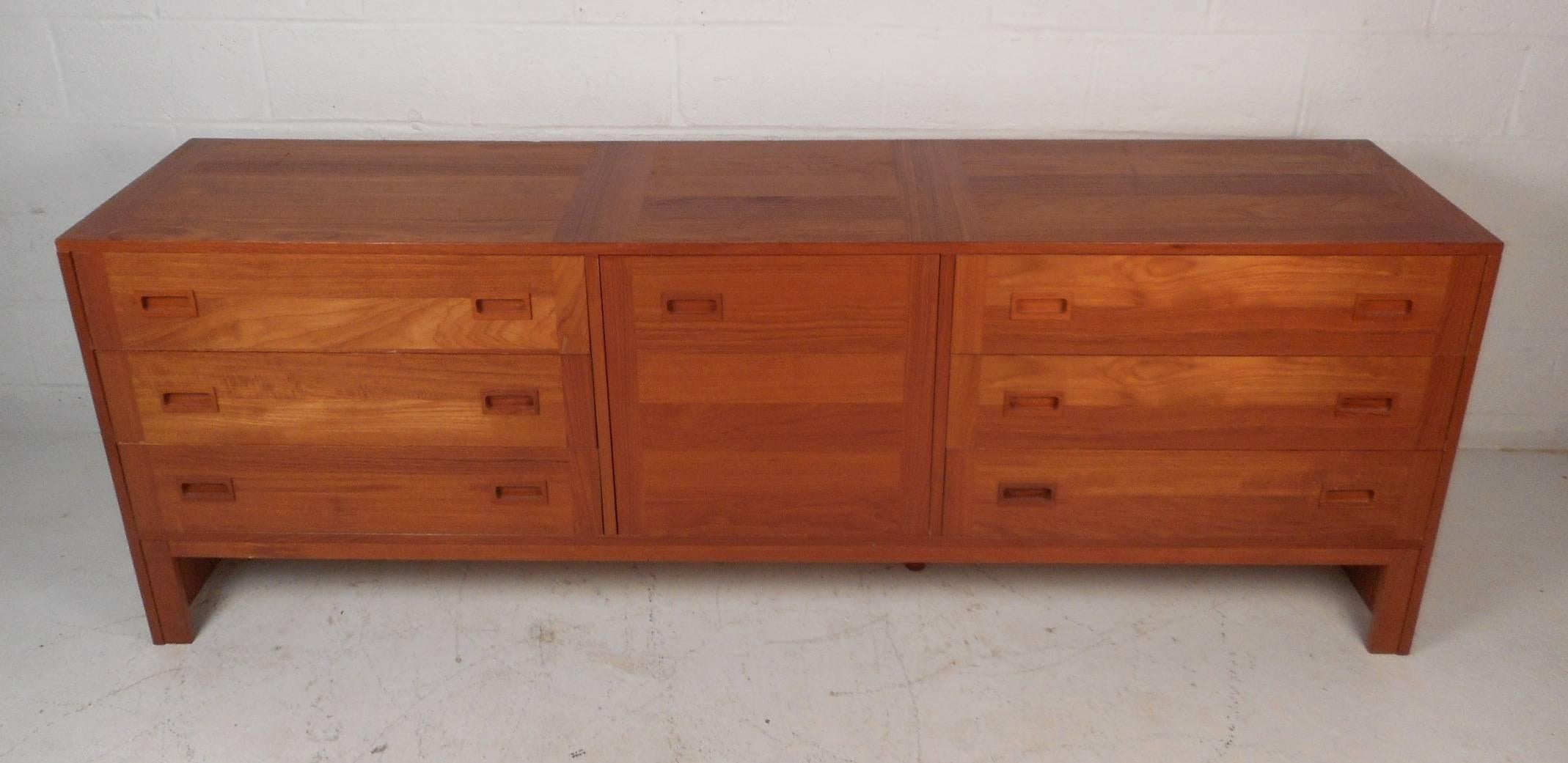 This beautiful vintage modern sideboard features an abundance of storage space within its six hefty drawers and compartment behind a cabinet door. Elegant teak wood grain and unique rectangular recessed drawer pulls add to the Mid-Century appeal.