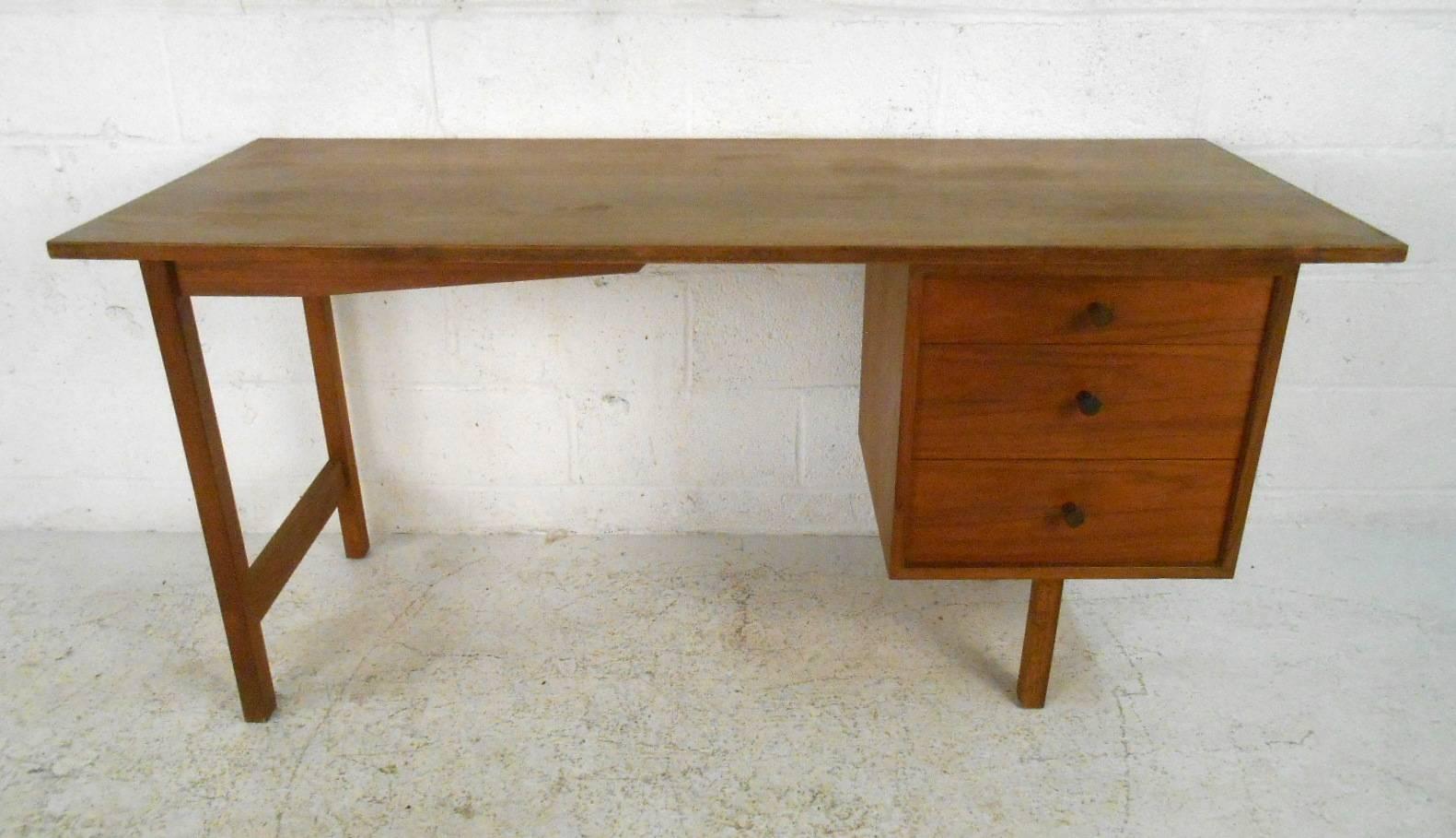 This gorgeous vintage modern desk features three hefty drawers and a large top ensuring plenty of work space. Quality craftsmanship with a finished back and a lovely walnut finish. Sturdy construction with straight lines and unique sculpted pulls