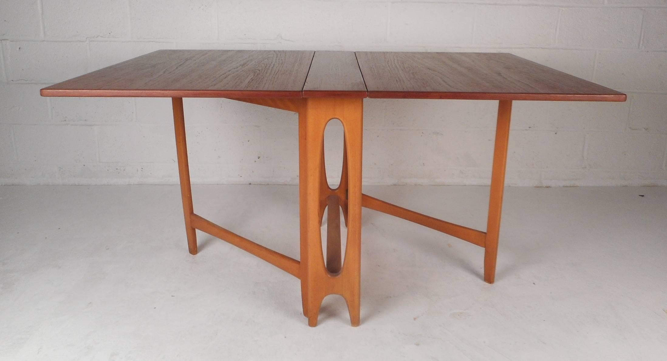 This beautiful vintage modern drop leaf dining table opens up to 56.75 inches wide. Unique design has gate legs that easily slide out ensuring sturdiness and style. This wonderful piece has a cut-out centre on the base and gorgeous wood grain