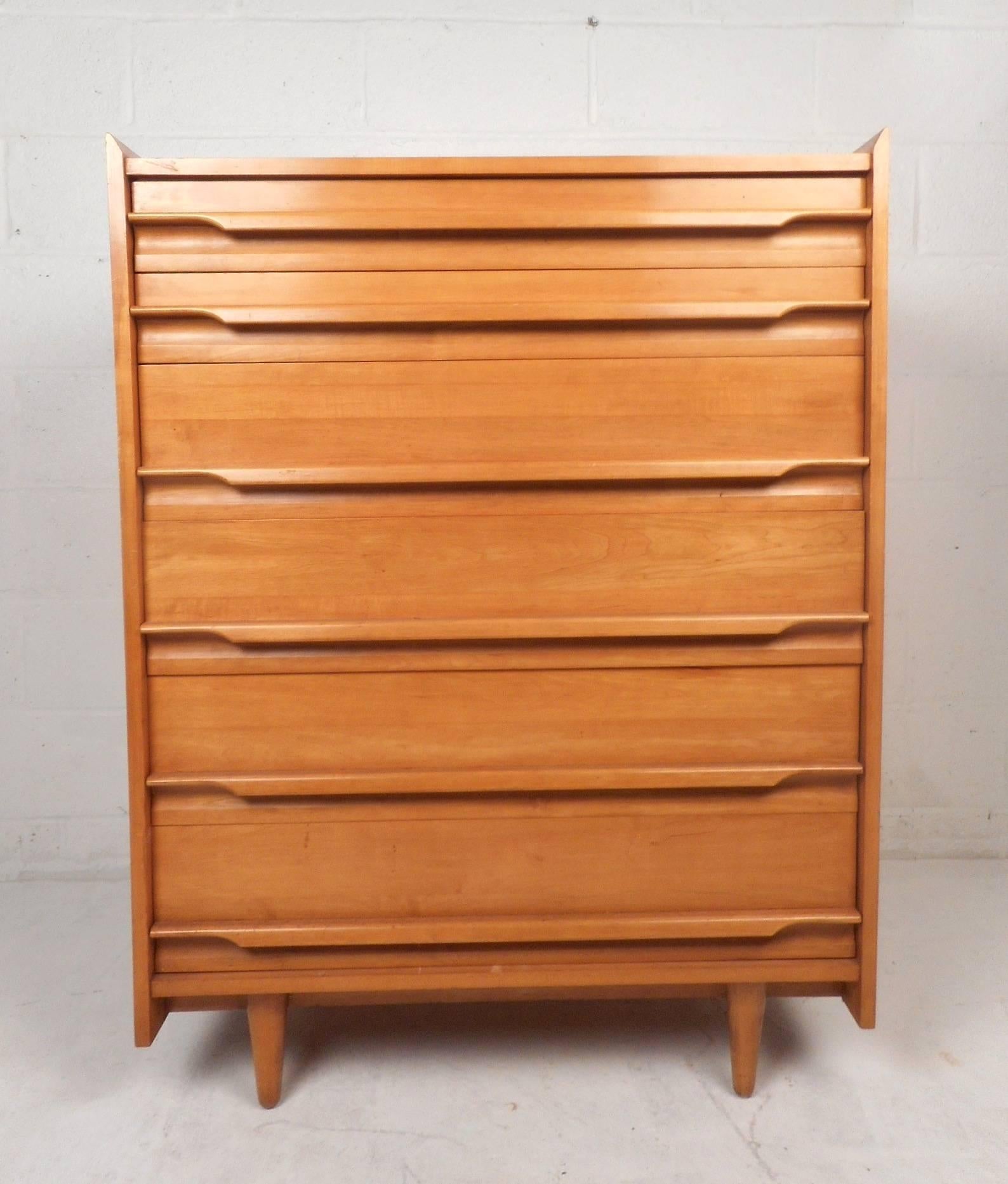 This stunning vintage modern dresser features six large drawers with unique sculpted pulls that stretch all the way across the centre of each drawer. Stylish design with raised edges along the top, tapered legs, and beautiful maple wood grain