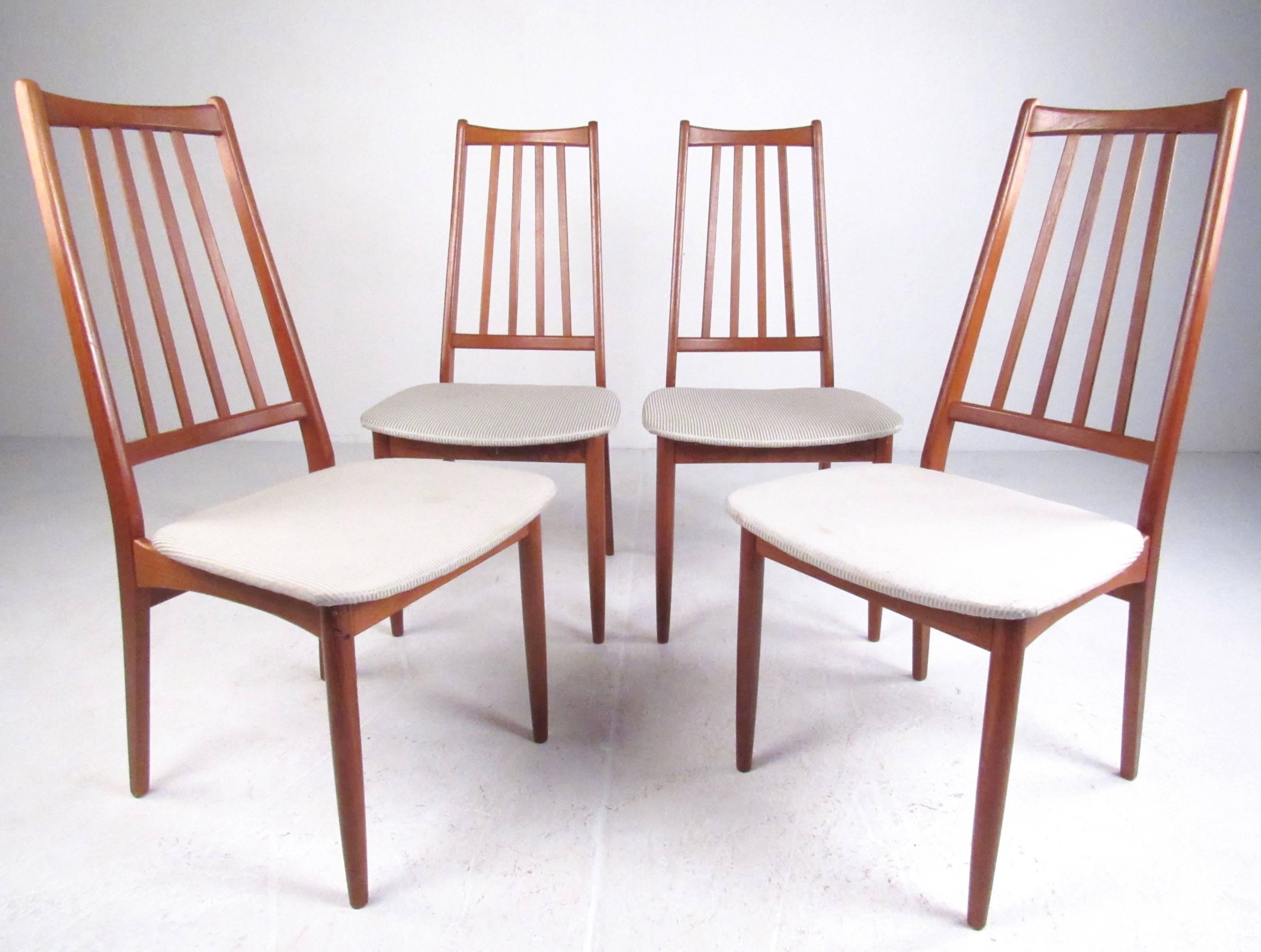 Cet ensemble de quatre chaises de salle à manger en teck aux lignes pures et élancées présente un design statuaire à haut dossier avec des rayons sculptés. Les sièges rembourrés forment un joli contraste avec la riche finition en teck, tandis que