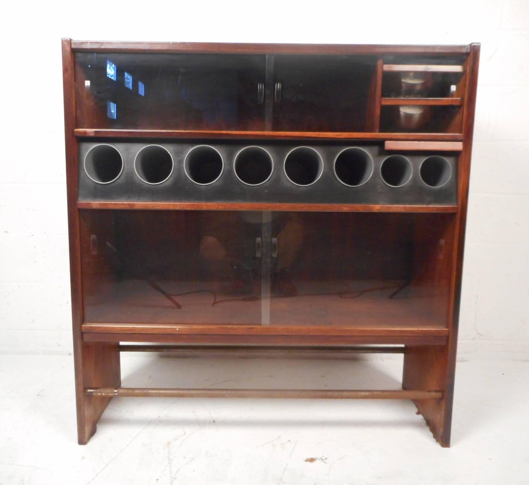 This beautiful vintage modern bar features a leather top and sliding glass doors. Sleek design with bottle holders, hidden ice buckets, and storage compartments. Wonderful bar made of rosewood with a metal kick rest on the bottom of each side. This