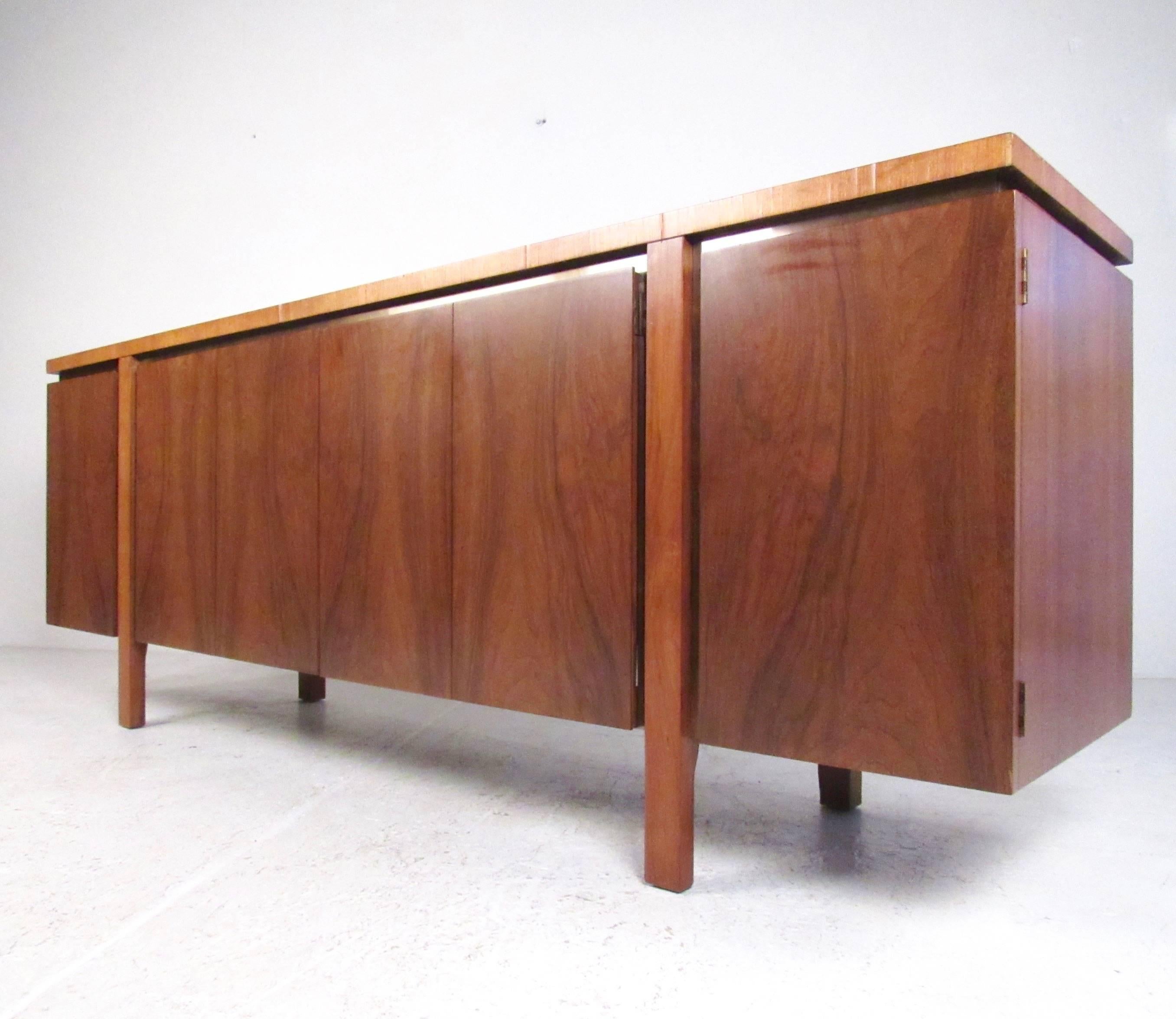 This beautiful Mid-Century Modern sideboard features unique TH Robsjohn-Gibbings design, including gorgeous matched wood finish, spacious storage cabinets, and stylized brass finish trim. This striking branded dining room server makes an impressive
