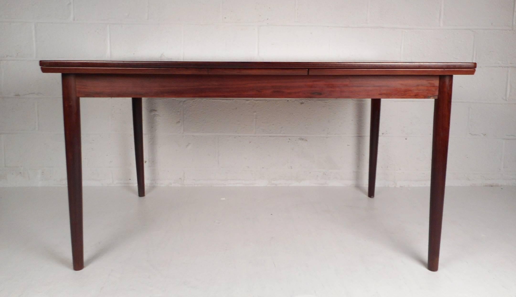 This beautiful vintage modern dining table features the ability to extend all the way to 97.5 inches wide from the original width of 55 inches. Elegant rosewood wood grain throughout and tapered legs add to the allure. Sleek design with hidden
