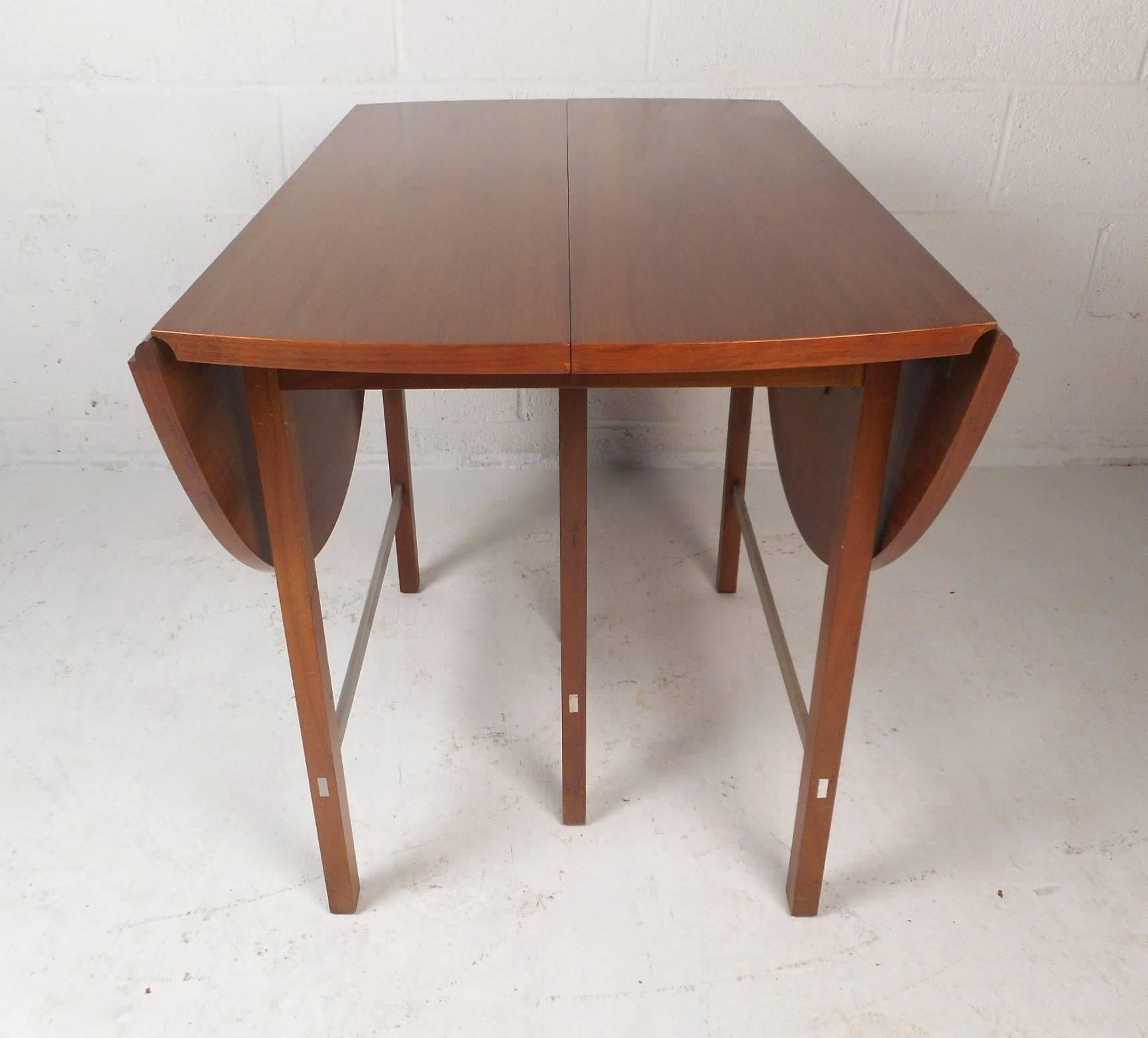 This gorgeous vintage modern dining table features a drop leaf design with three additional leaves allowing this table to go from 25.75 inches wide all the way to 90 inches wide. The sleek design has unique aluminum stretchers and lovely walnut wood