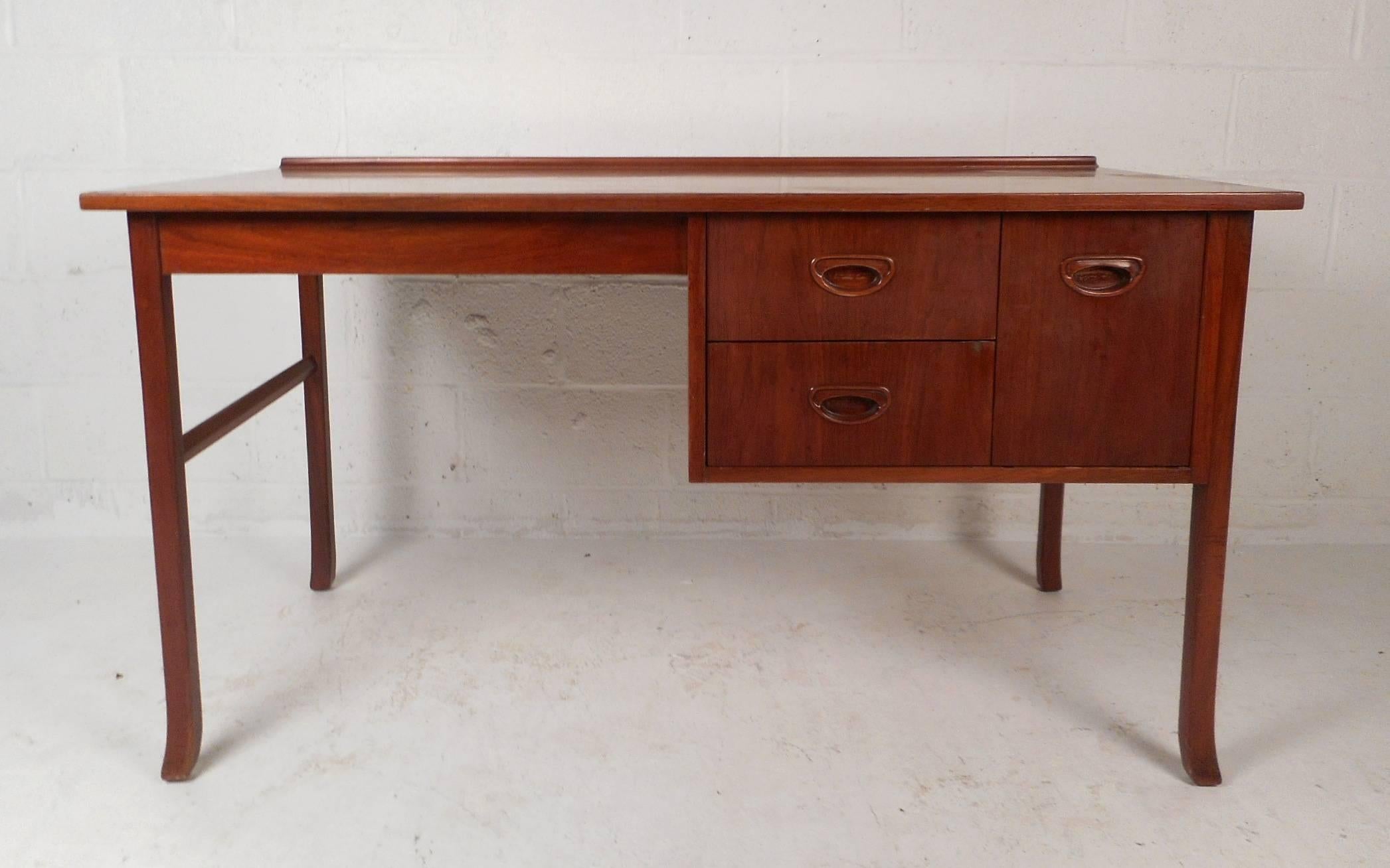 This gorgeous vintage modern desk features a unique raised top along the back and sculpted feet. Sleek design with unusual recessed pulls and a wonderful vintage teak finish. This case piece ensures plenty of room for storage within its three hefty