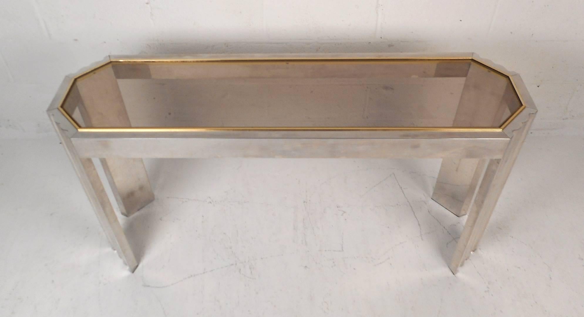 This beautiful vintage modern hall table features a smoked glass top with brass trim running along the edges. Sleek design has unique legs with louvered indents running vertically and bevelled sides. This eight sided mid-century table is versatile