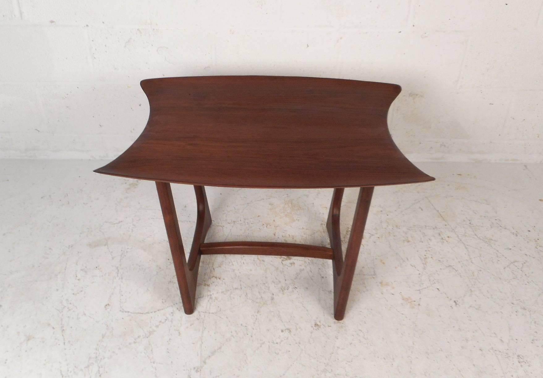 This gorgeous vintage modern walnut end table features a sculpted top and unique curved sled legs. The sleek design has an unusual top with smooth rounded edges along the front and back. Quality craftsmanship has a sturdy base with a stretcher