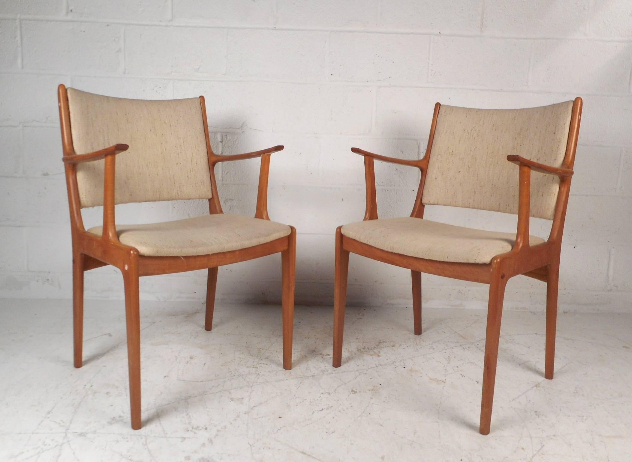 This gorgeous pair of vintage modern dining chairs feature unique angled arm rests and plush beige upholstery. Sleek and sturdy design with a high upholstered back rest and elegant teak wood grain throughout. The sculpted arm rests and soft fabric