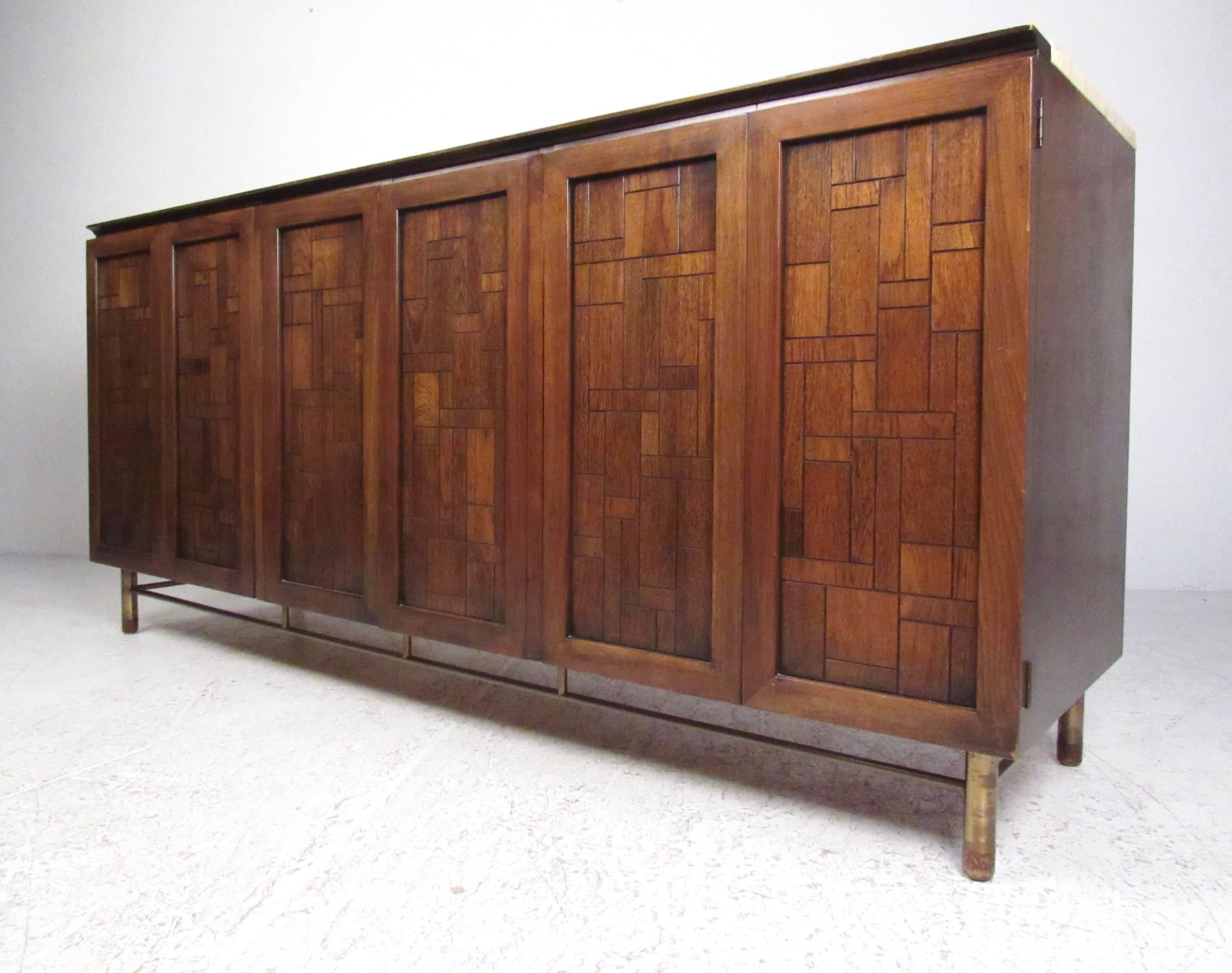 This stylish vintage modern sideboard features sculptural brutalist style cabinet doors, brass legs, and travertine top to create a truly unique mid-century addition to any interior. Impressive and substantial storage piece perfect for home or