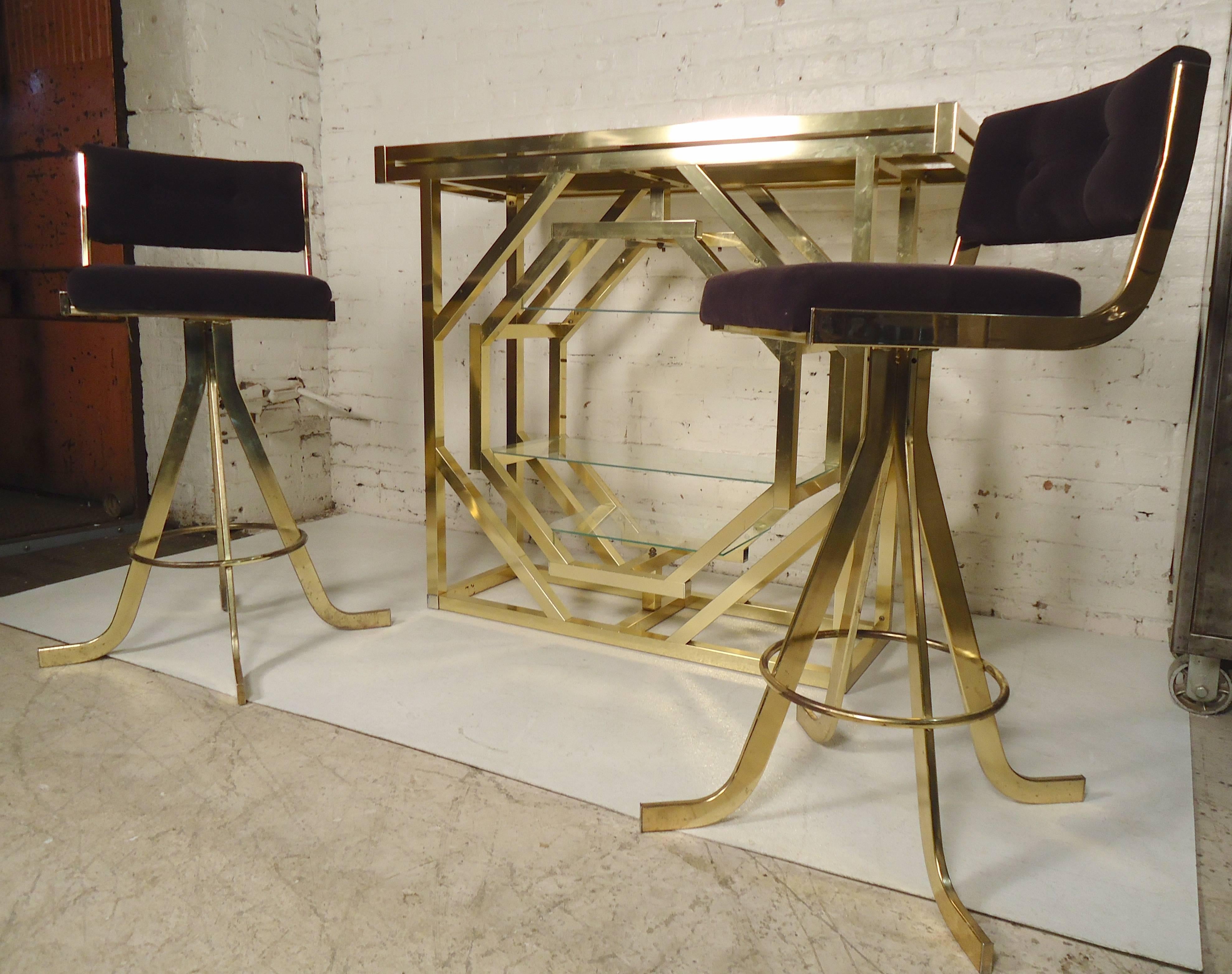 Beautiful brass dry bar with two stools. Bar has a black glass top and unusual rotating shelving unit. Stools have soft purple fabric.
Bar: 49.5