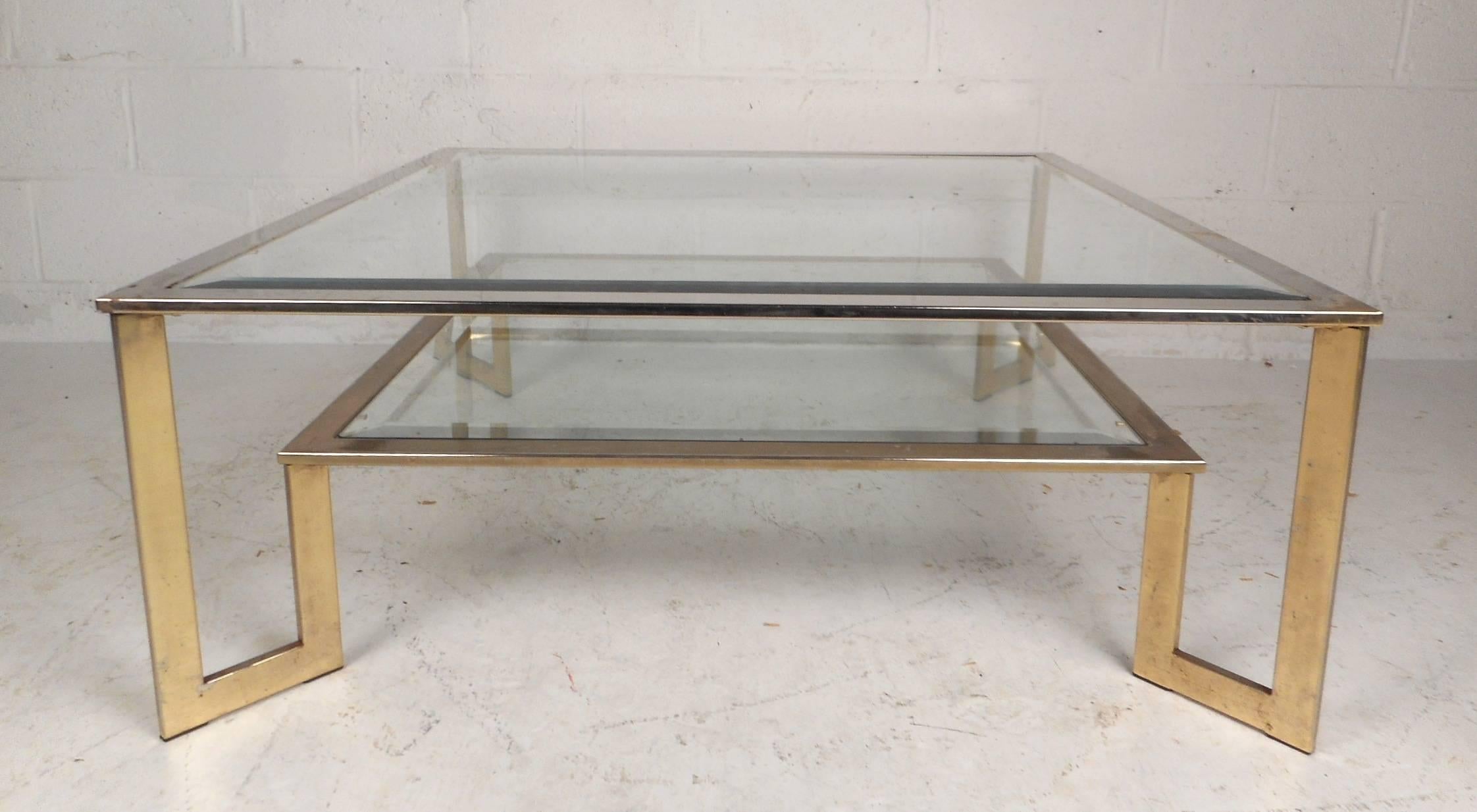 This unique vintage modern square cocktail table features a large glass top with beveled glass and a smaller lower glass tier. Sleek design with a sturdy flat bar metal frame joining both table tops. This unusual table allows for extra storage or