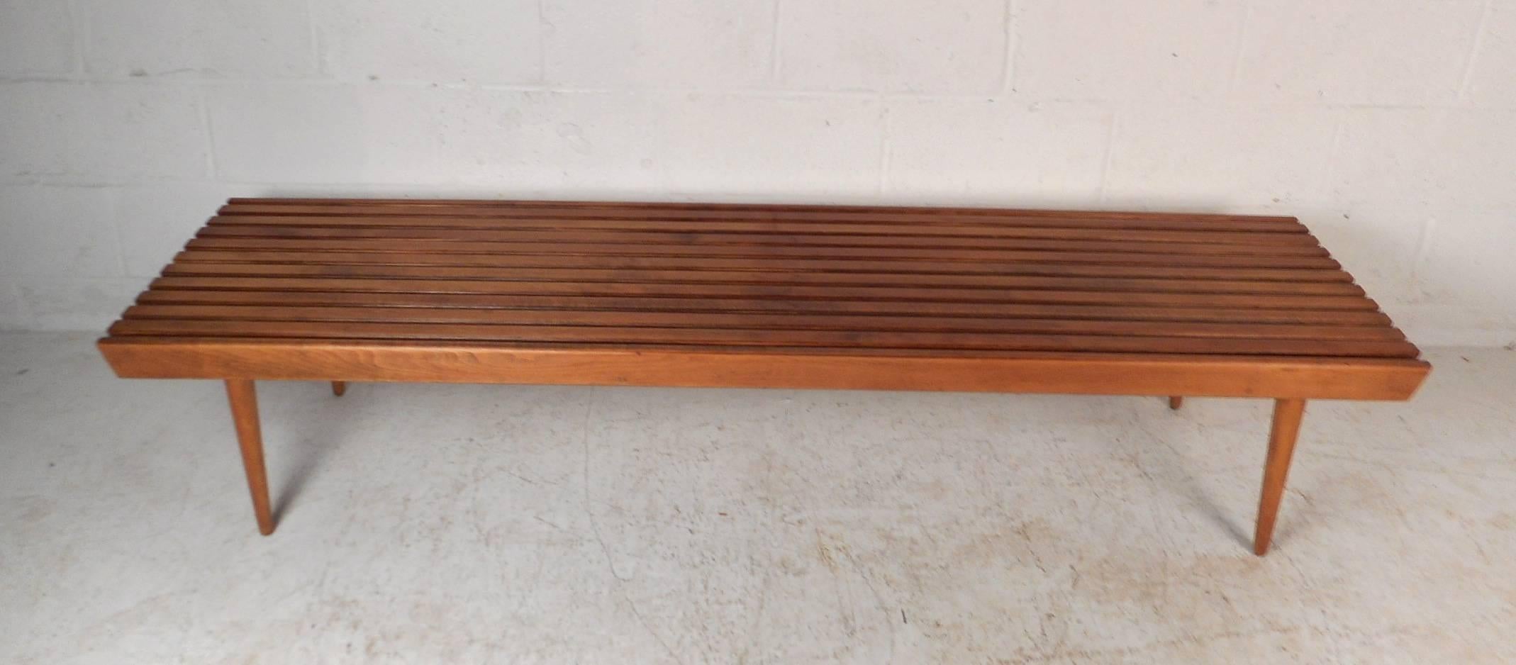 This beautiful vintage modern slat bench is 72 inches wide and features tapered legs. Sturdy construction with a wonderful light walnut finish throughout. This stunning midcentury piece functions as a coffee table or a bench. Perfect addition to any