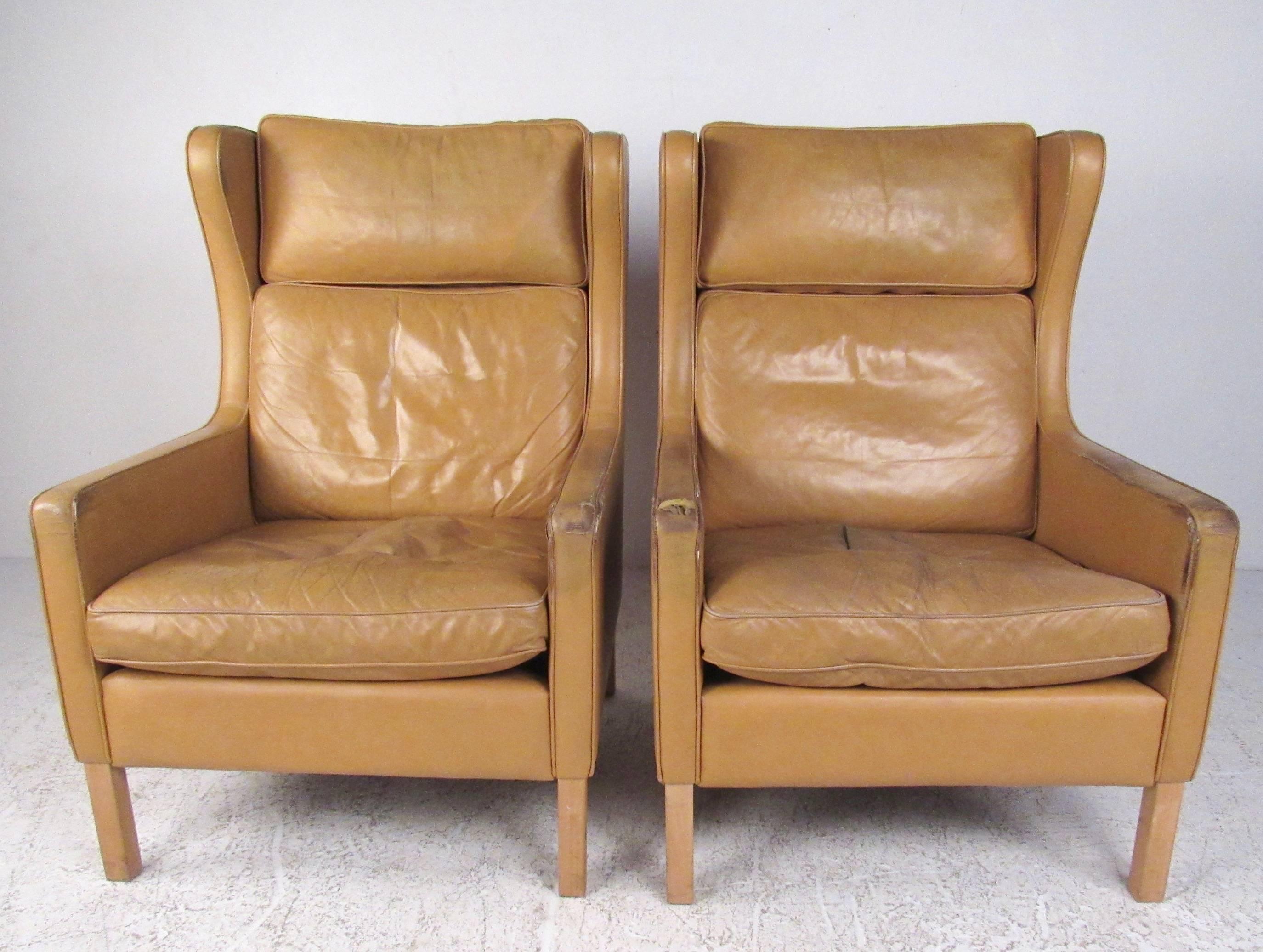 This pair of Børge Mogensen wingback lounge chairs for stouby come paired with matching ottomans. Vintage leather upholstery is worn, but this statuesque pair of Scandinavian Modern lounge chairs make an impressive addition to any seating
