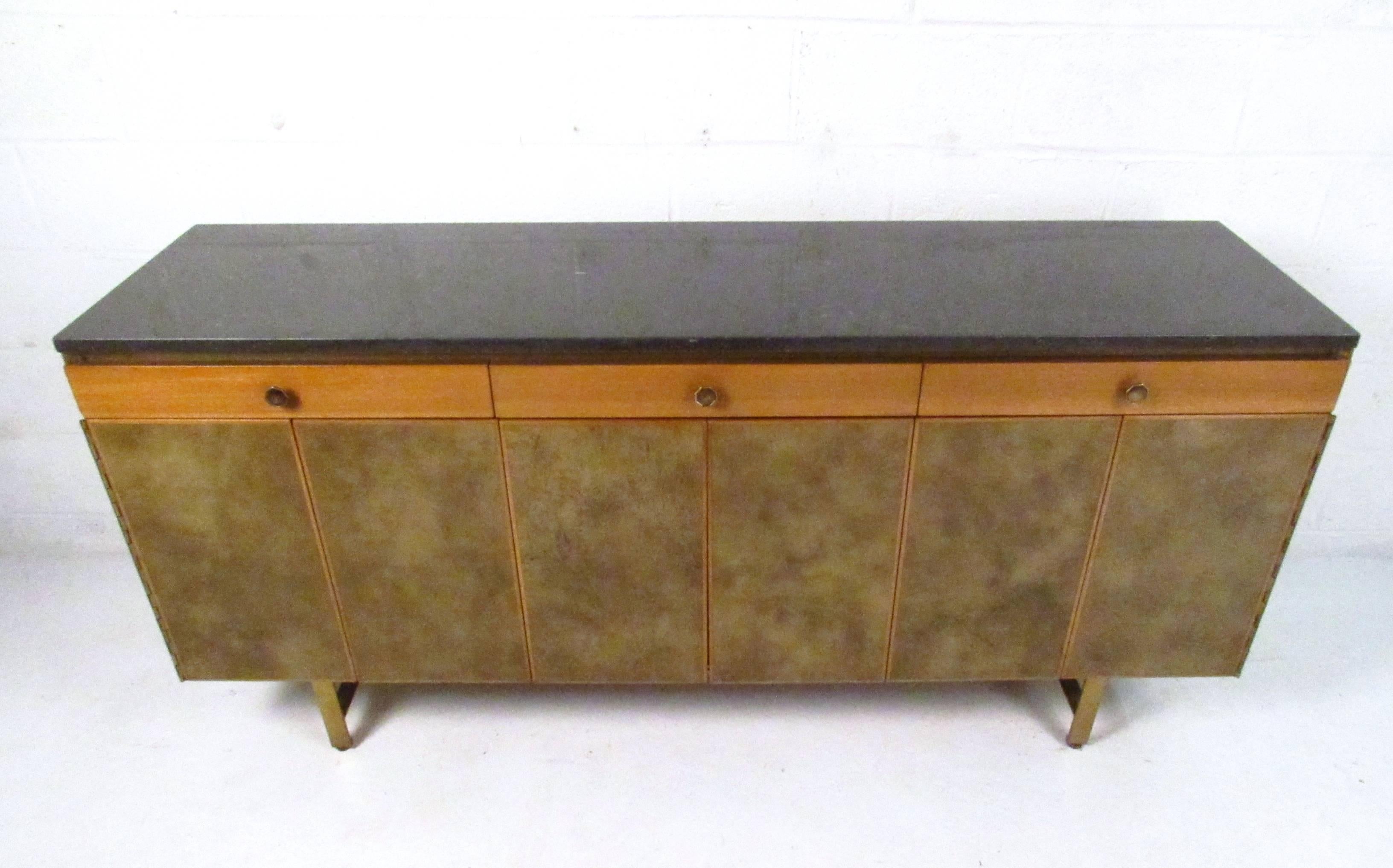 This beautiful vintage McCobb sideboard features a stylish black travertine top, unique legs and pulls and leatherette covered tri-fold cabinet doors. Original manufacturer's label still intact, internal drawers lined with same leatherette. Please