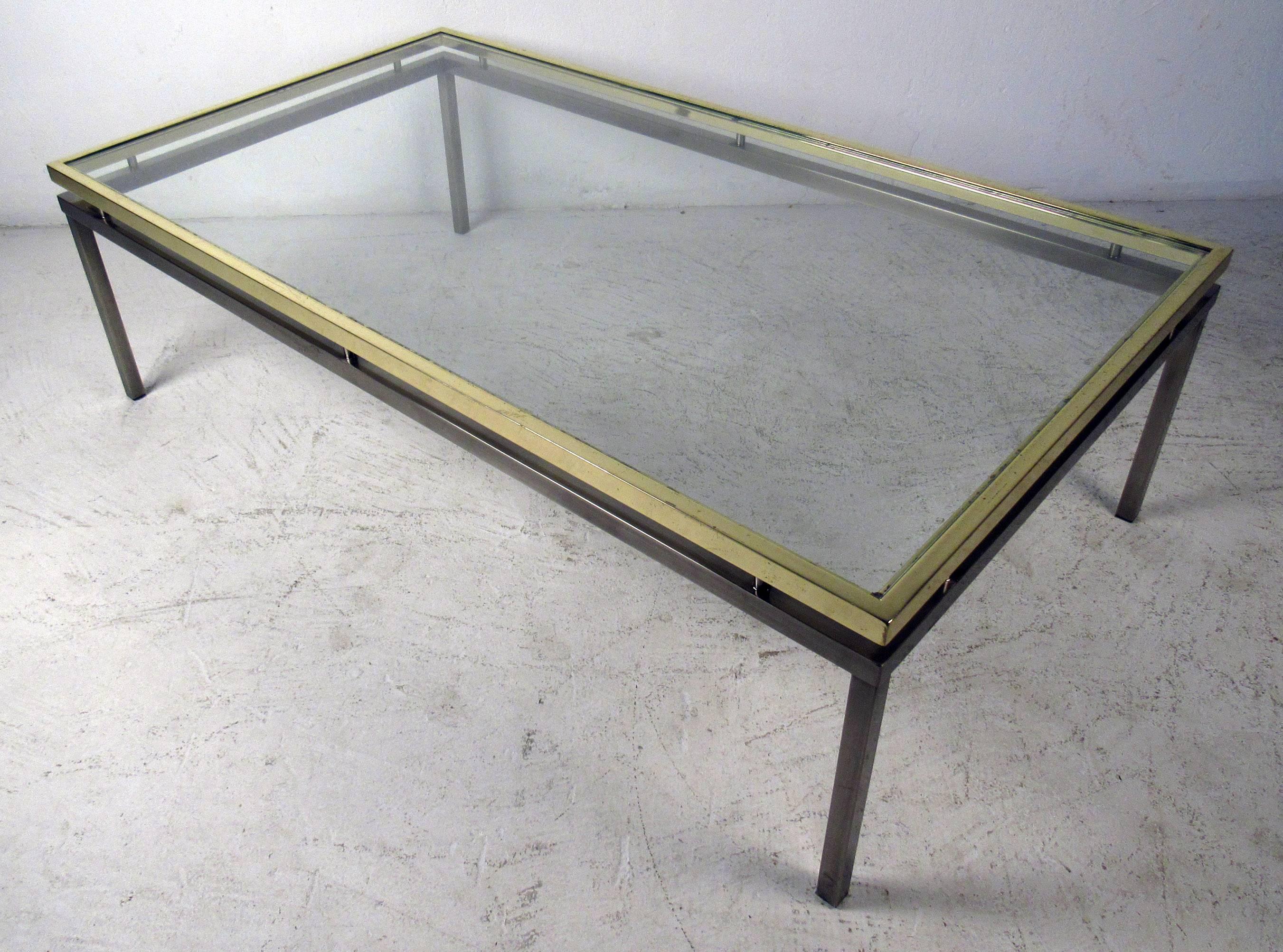 Mid-Century Modern coffee table featuring sturdy chrome and brass base with a glass top. A stylish two-tone piece with a slightly raised top and large rectangular glass. Designed by Mastercraft, this is the perfect vintage cocktail table for home or