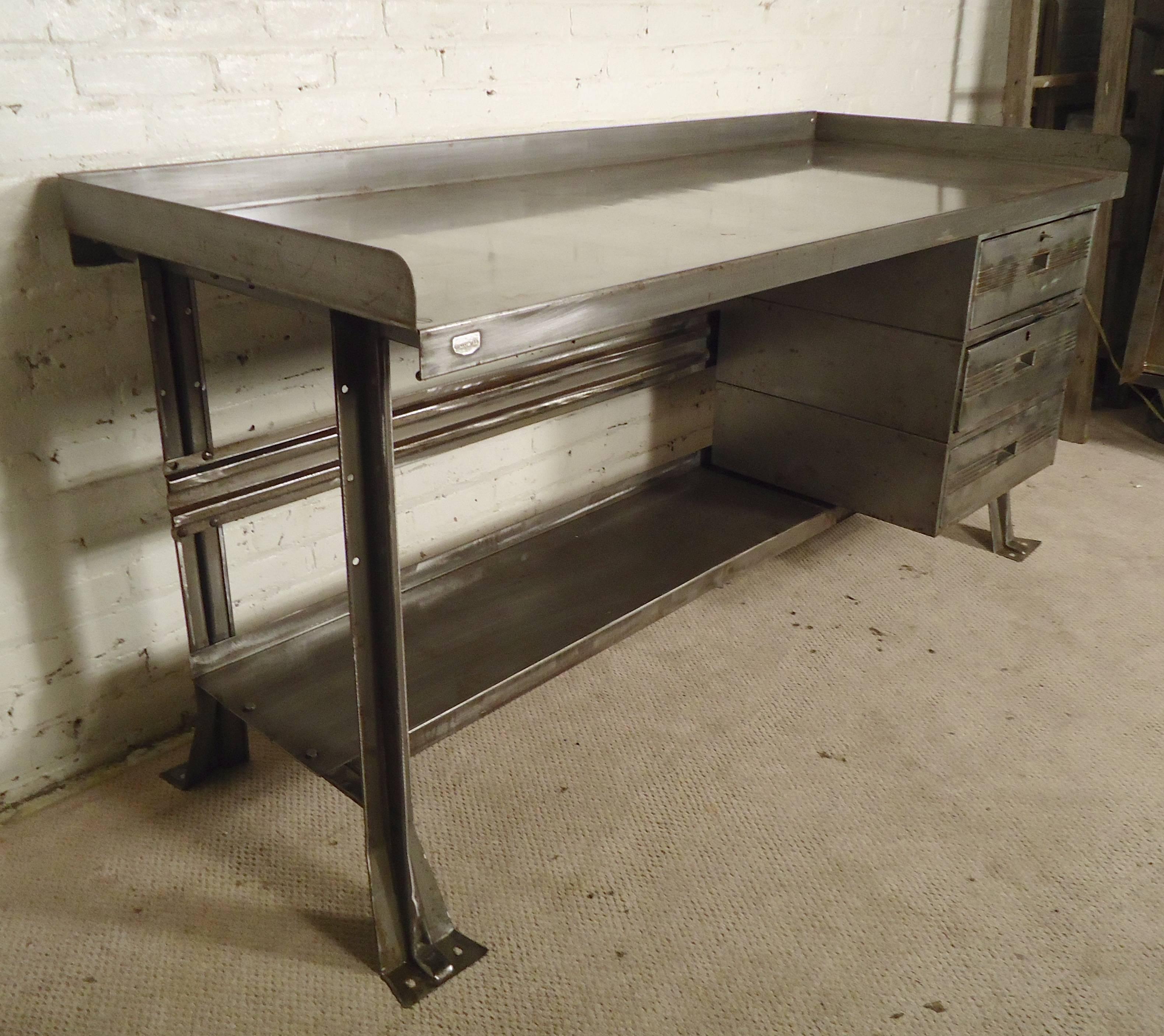 Massive industrial metal artist desk, completely refinished in a bare metal style. Long desk top, three drawers and footrest that can serve as additional storage space. Works with a 27