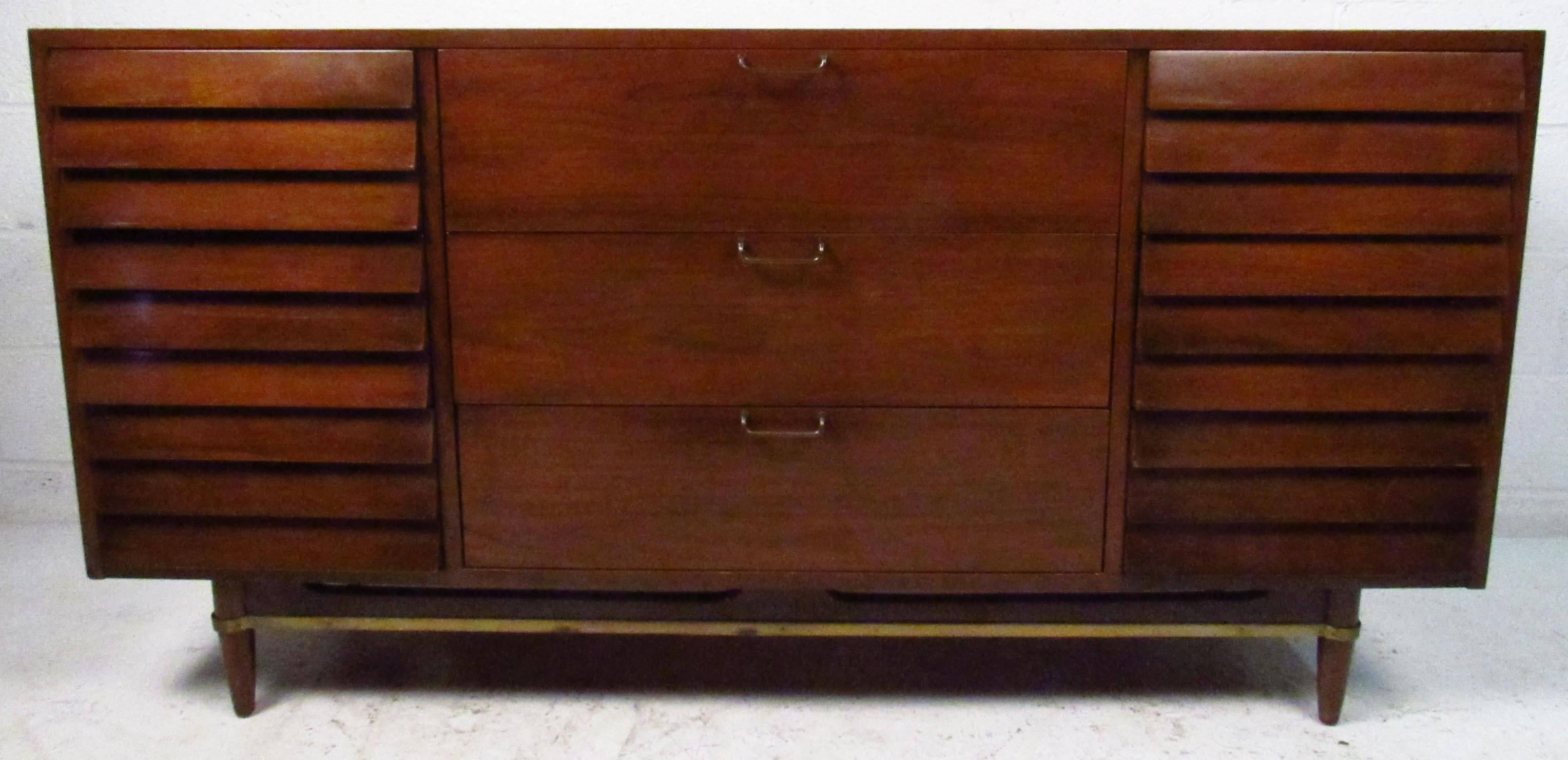 This stylish vintage modern dresser features louvered front with brass trim and sculpted handles. Designed in the 1970s by Merton Gershun for American of Martinsville, this unique nine drawer bedroom dresser makes an impressive addition to any