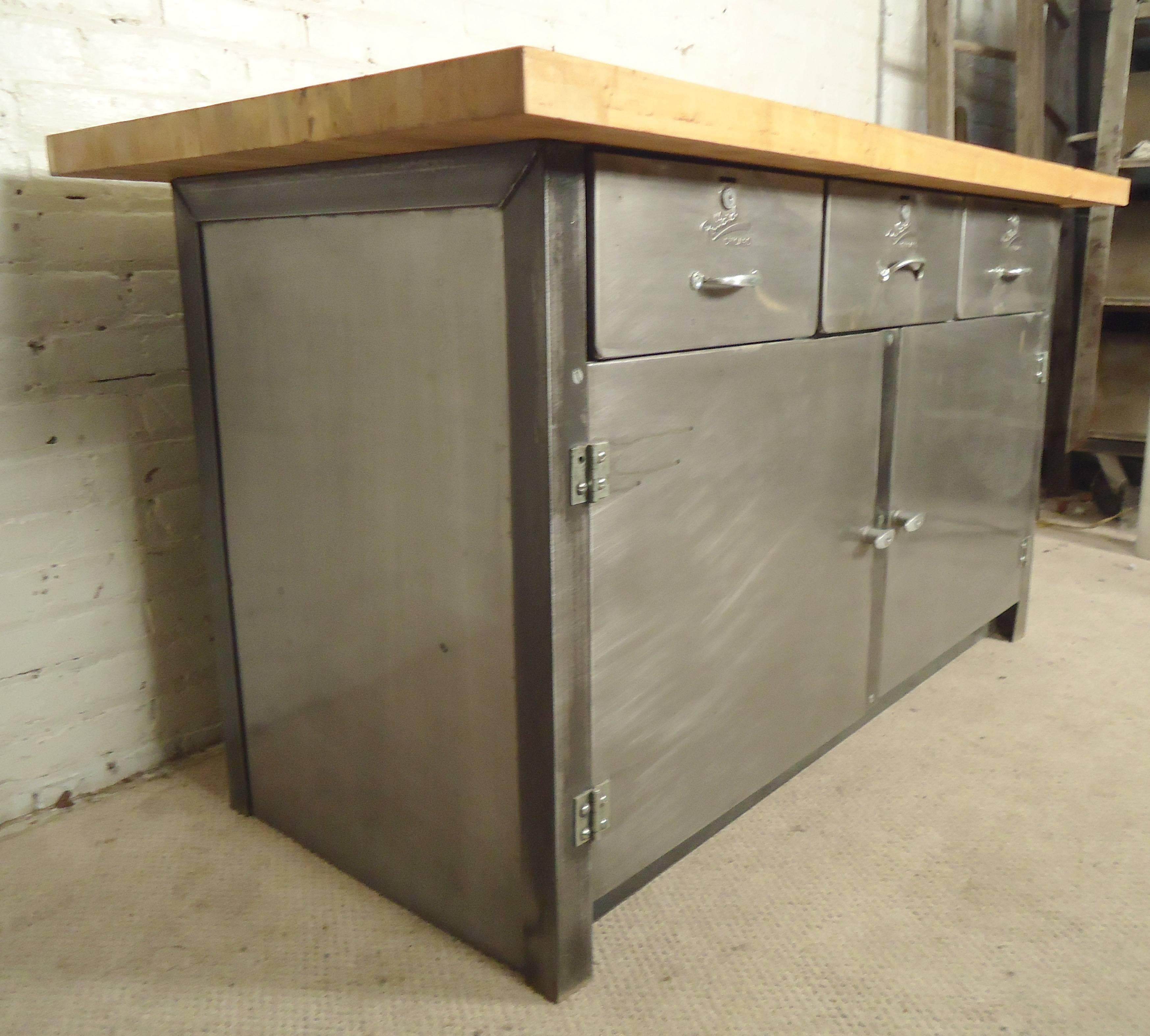 This large factory table features a thick butcher block top on a refinished metal base. Three drawers and two wide cabinets for storage, restored in a bare metal style finish. Each has a distinct discoloration on the top.
(Two