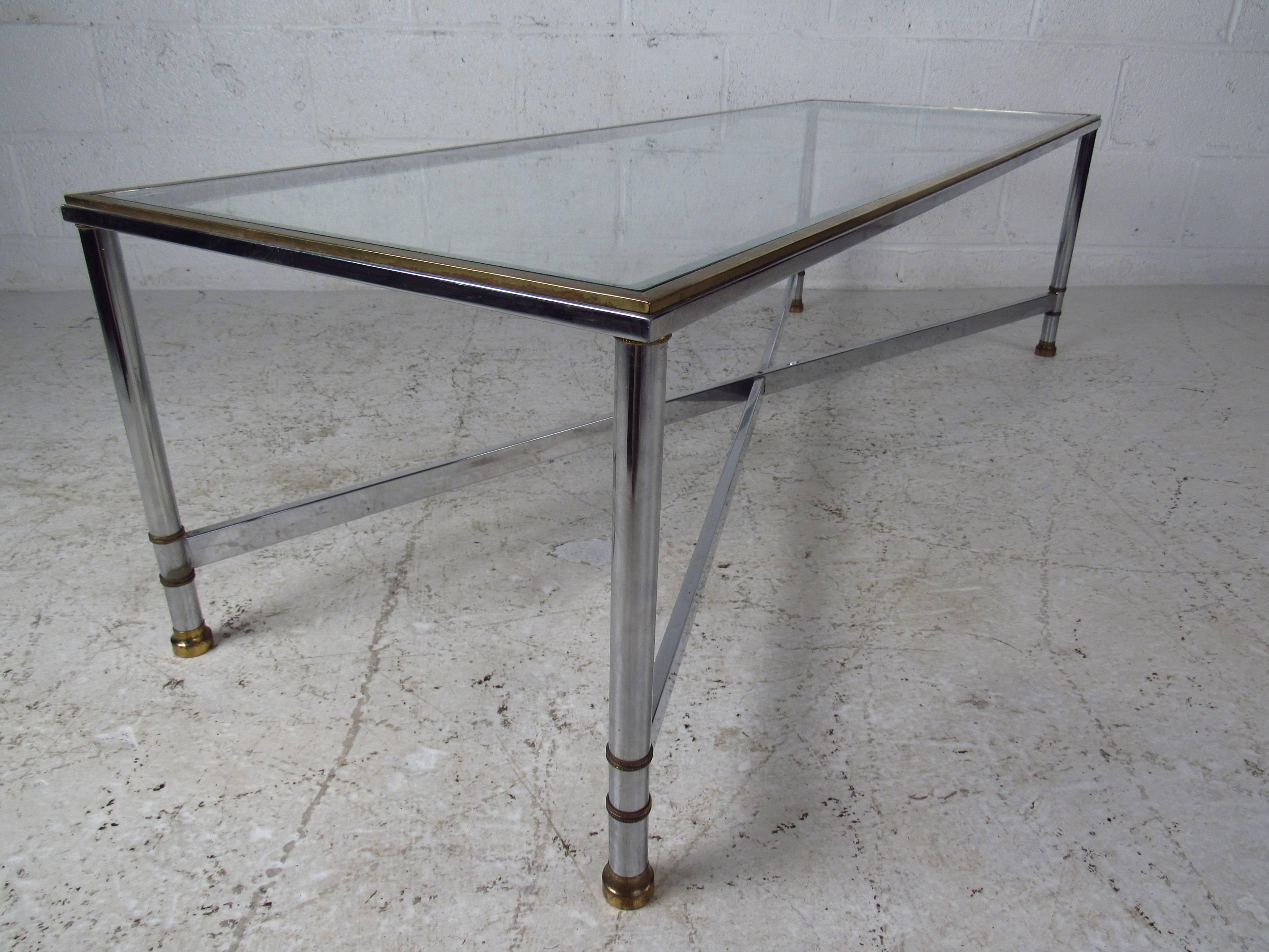 This beautiful vintage glass coffee table has a unique X-base, adding both style and stability. The chrome trim along the edges, tubular chrome legs, and rectangular glass top add to the mid-century appeal. This Maison Jansen style cocktail table