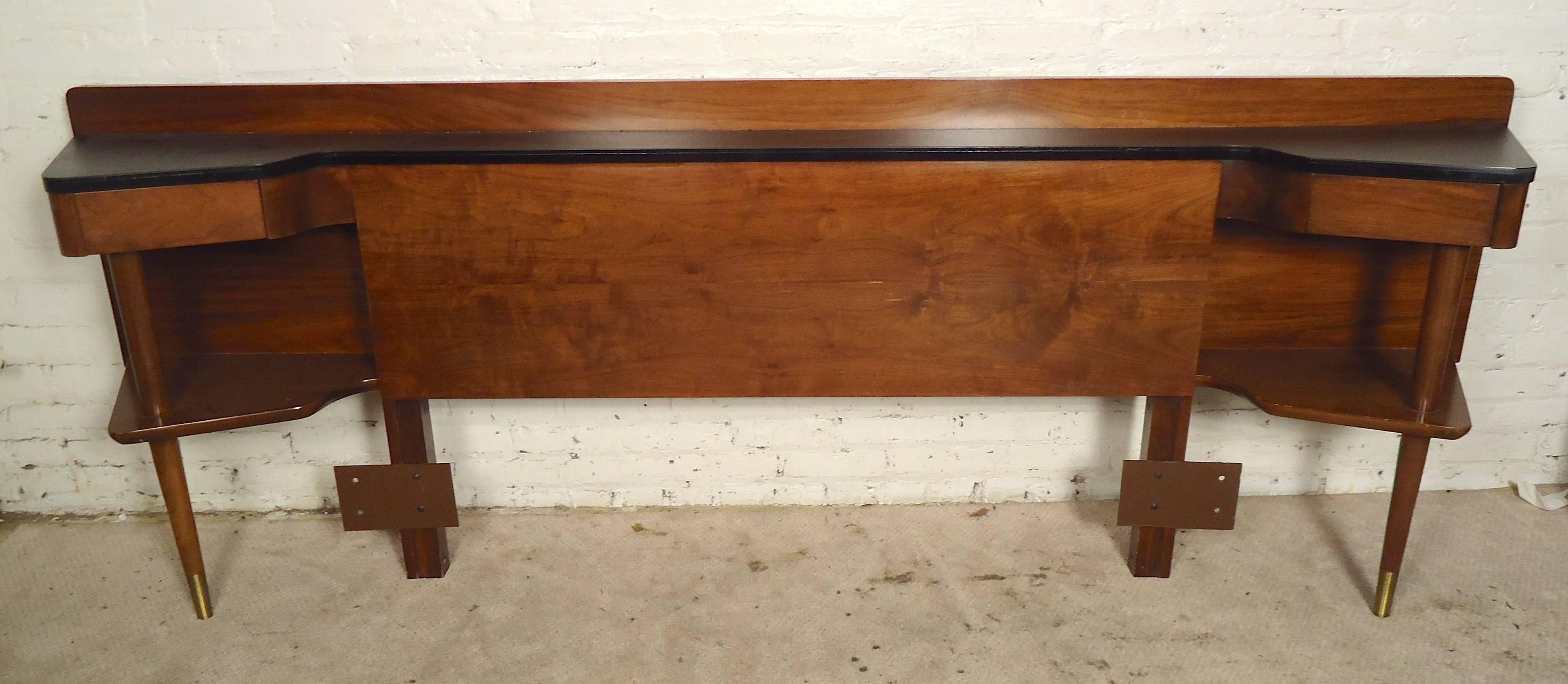 Queen size headboard made by American Of Martinsville. Walnut grain with faux leather top and brass detailing. Long shelf for books, two side drawers and lower shelf for storage.
Matching dressers available.
[62