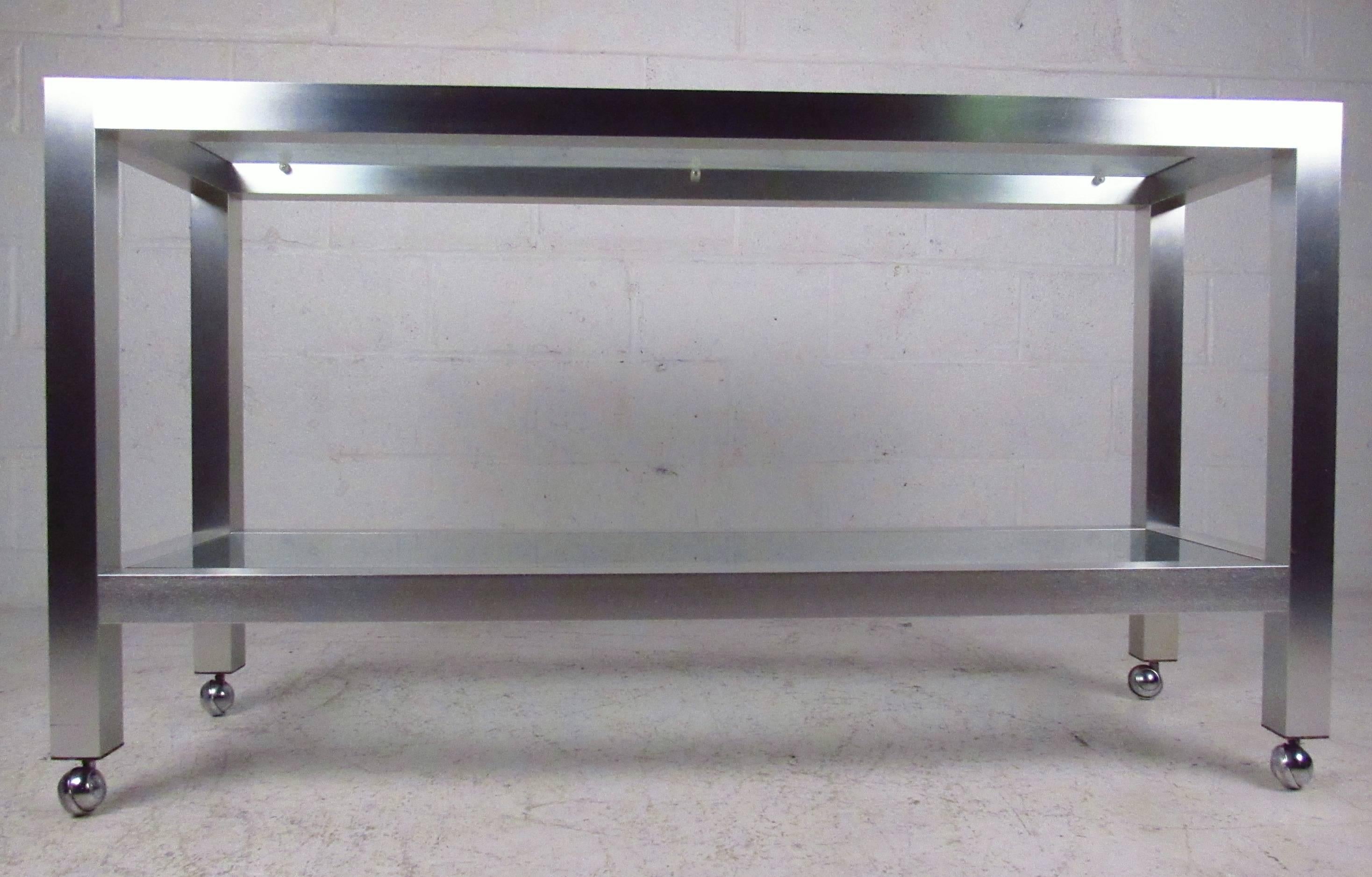Mid-century aluminum console table with two glass shelves. Rolling casters allow easy mobility. Brass corner pieces accent the brushed chrome look.

(Please confirm item location - NY or NJ - with dealer)

