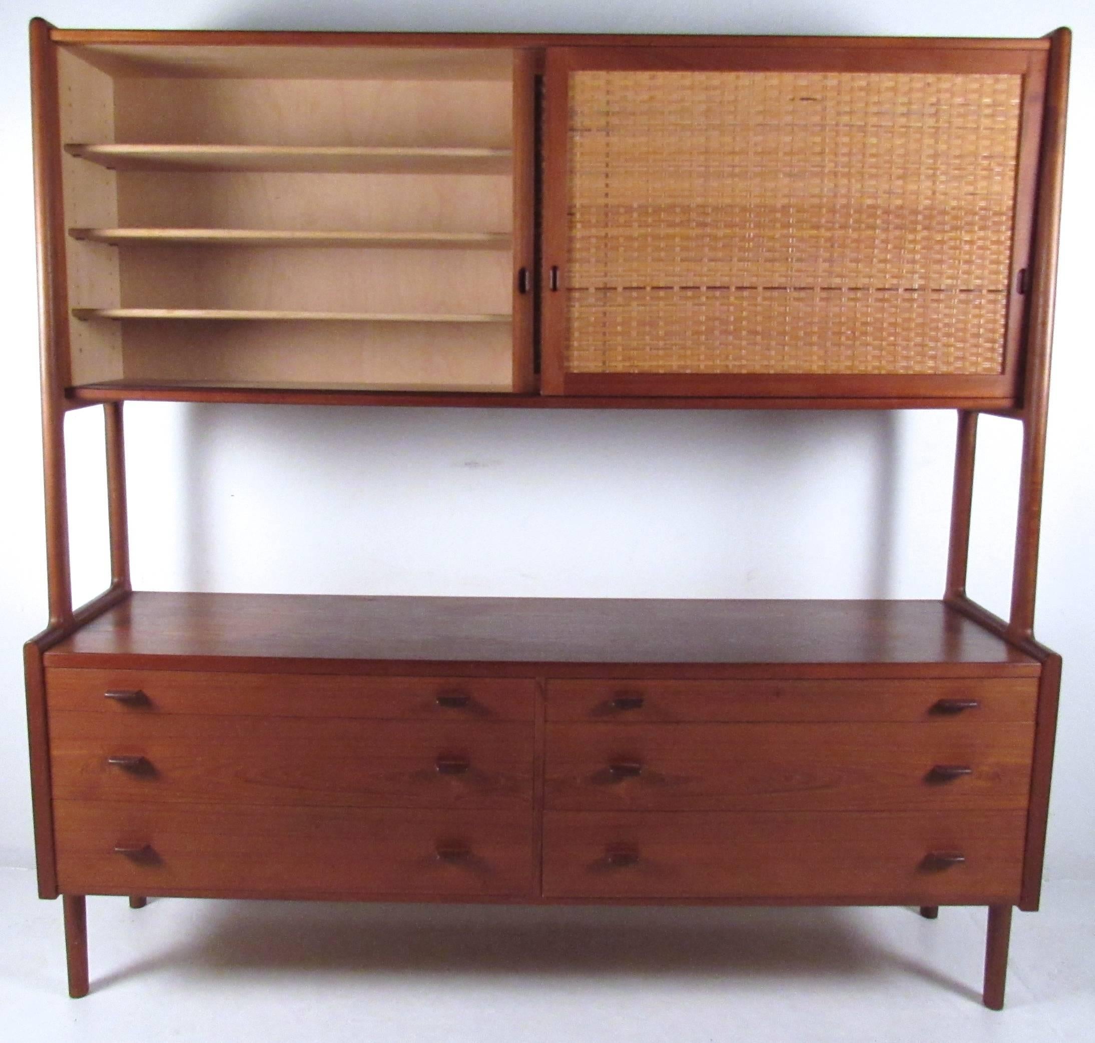 This beautiful Mid-Century sideboard features the unique two-tier design of Hans Wegner, combining quality teak construction with spacious storage options for any setting. Adjustable shelves, unique vintage finish and cane front sliding door