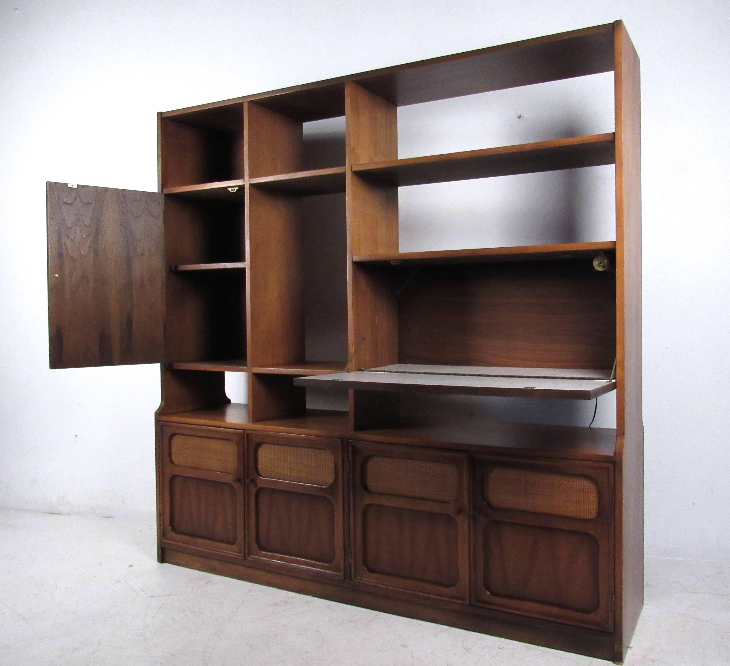 This lovely vintage wall unit offers a stylish combination of storage and display options including backlight drop front dry bar, reversible panel cabinet storage and ample open shelf space. Wonderful natural wood finish is offset by cane front