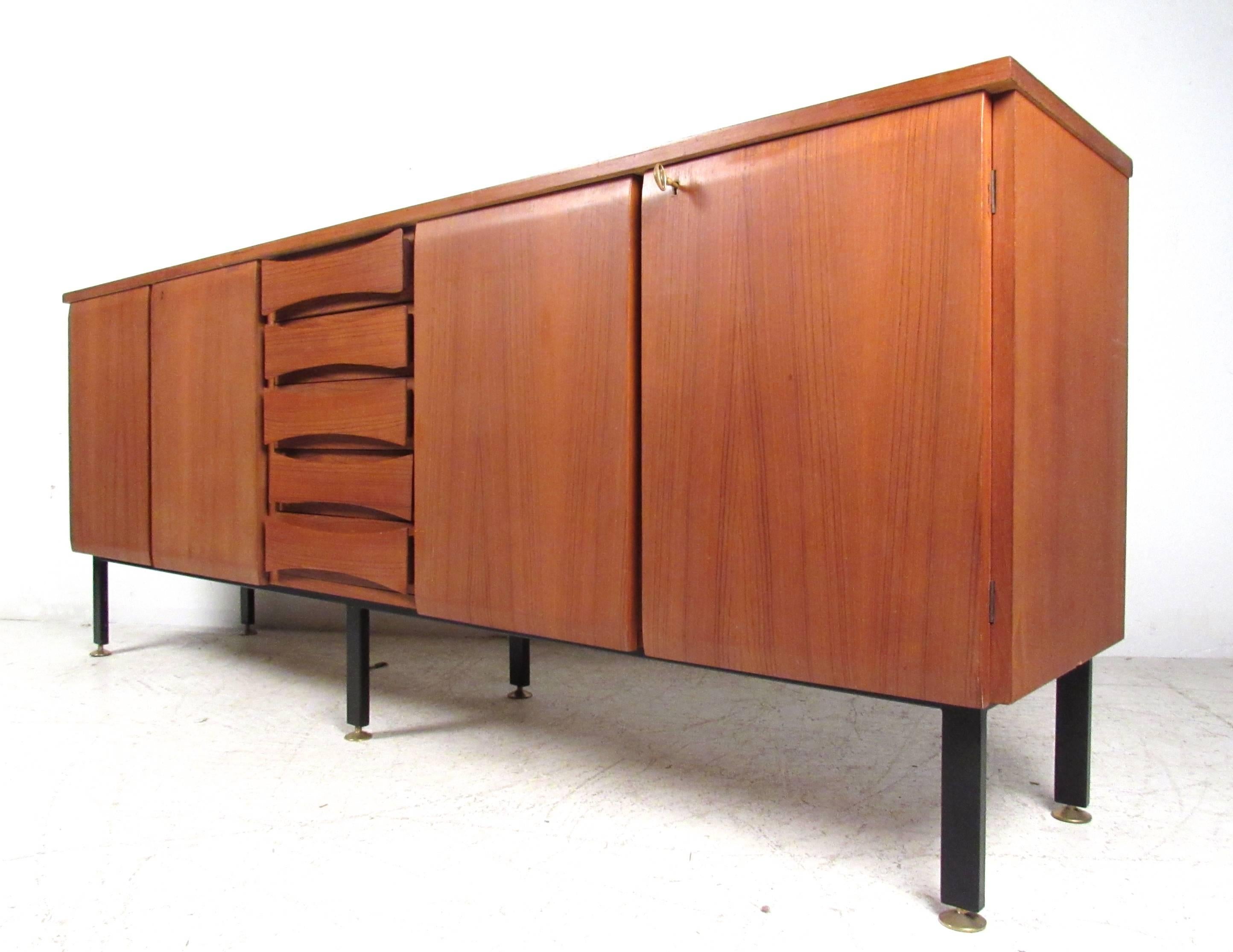 This stylish teak sideboard makes an impressive addition to any home or office decor. Sturdy metal legs, spacious locking cabinets and center drawers for added organization make this an efficient and practical piece. Please confirm item location (NY