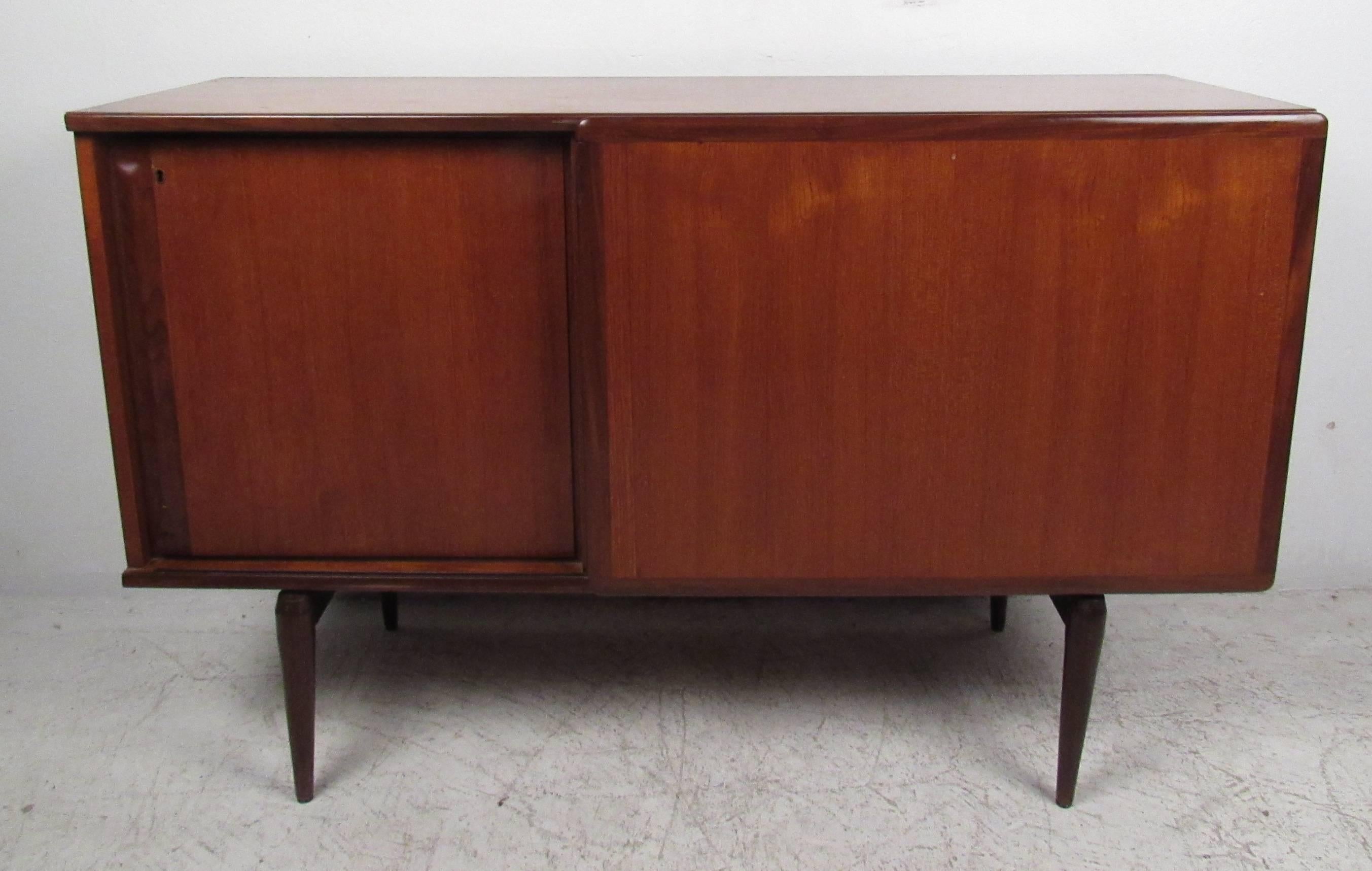 Unique Danish modern sliding door cabinet with adjustable shelves and rich teak finish. A petite design with tapered legs and plenty of room for storage within its large compartments. Please confirm item location (NY or NJ) with dealer.