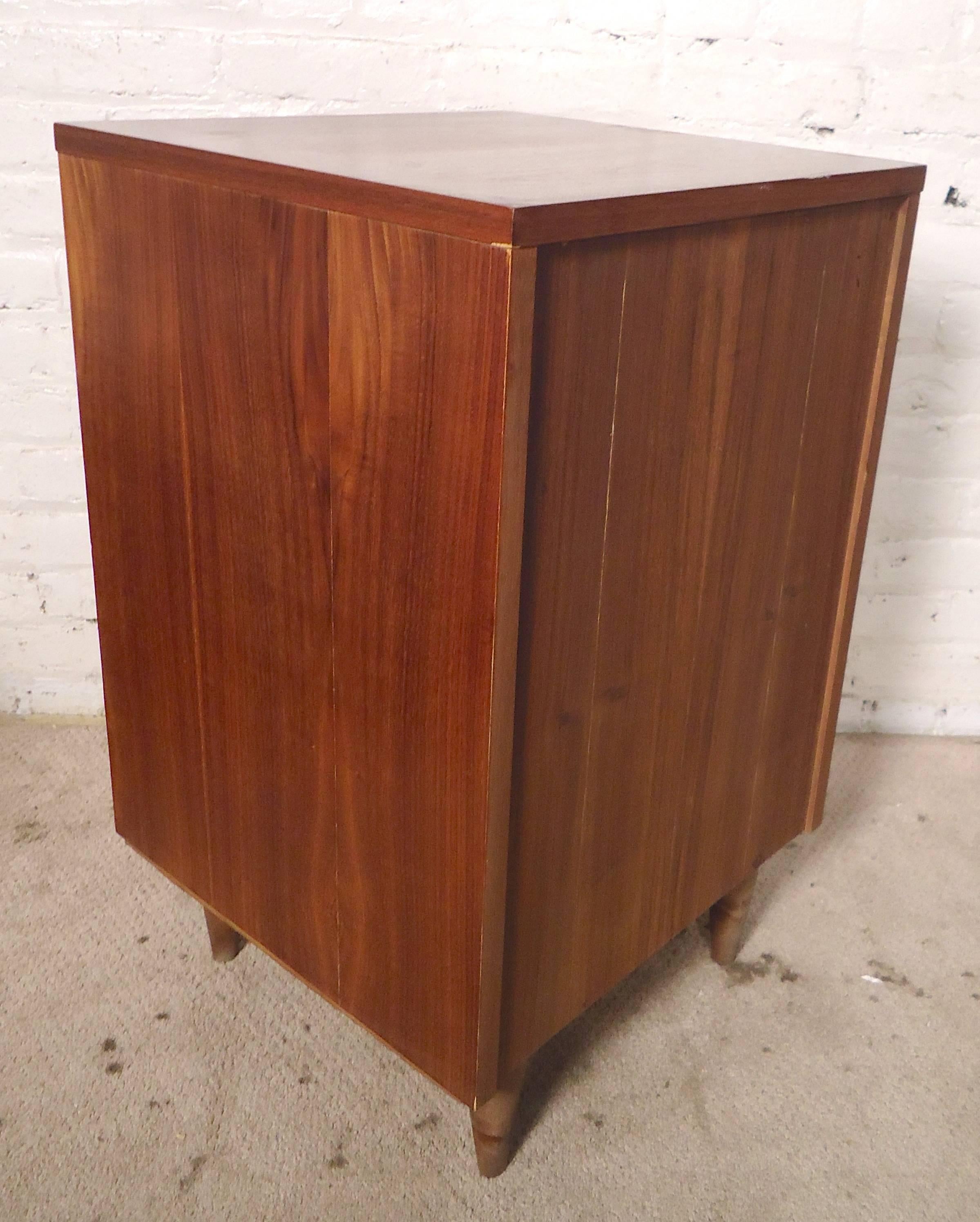 Unusual size cabinet with warm walnut wood grain. Tapered legs, white pulls, two drawers. Great for office or bedside storage. (Please confirm item location - NY or NJ - with dealer.)