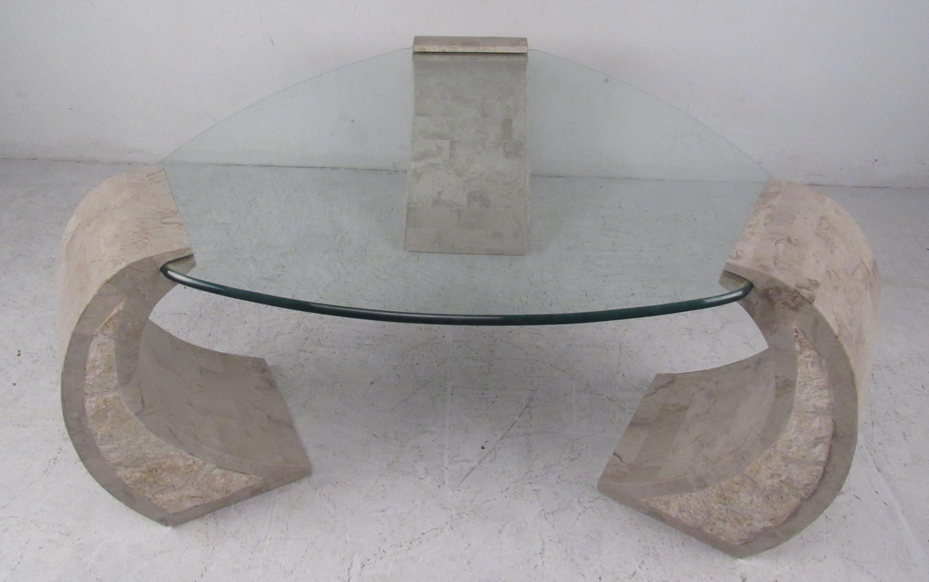 Table de cocktail triangulaire de style Maitland-Smith avec des supports uniques en forme d'arc en pierre tessellée. Table de cocktail élégante avec une finition bicolore unique et un plateau en verre profilé. Veuillez confirmer la localisation de