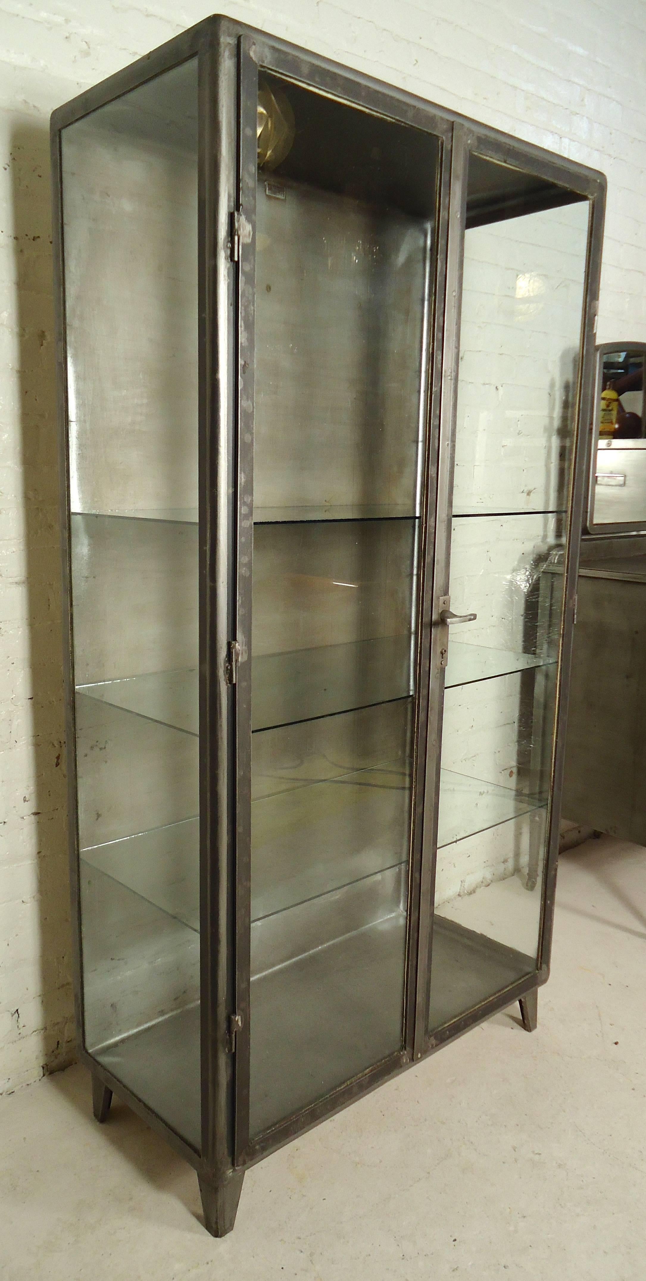 Pair of refinished metal cabinets with three glass sides and glass shelving. Each cabinet can accommodate nine shelves; handle locking system, refinished in a bare metal style finish. One cabinet features coat hooks.

(Please confirm item location